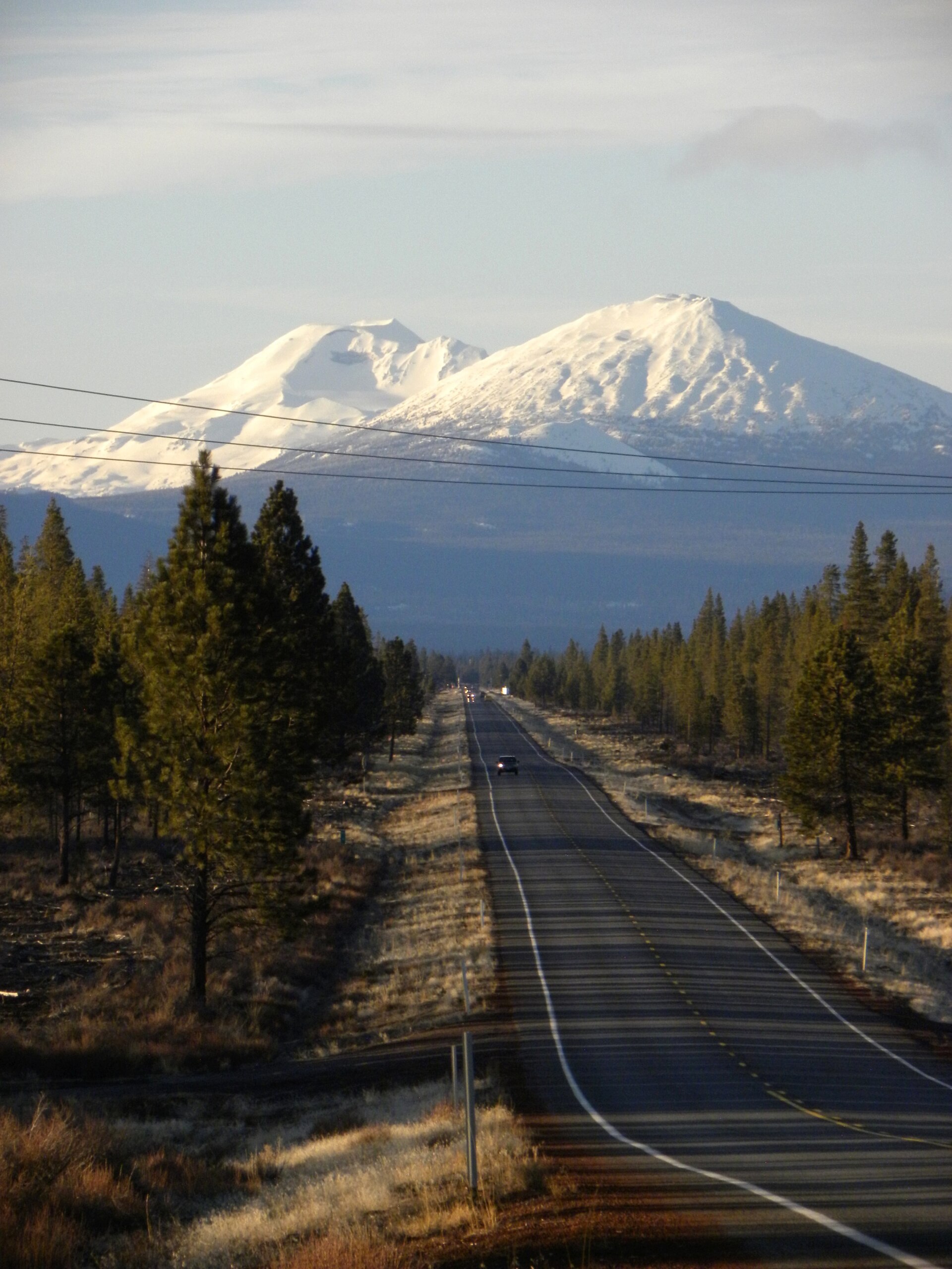 Snow-capped Cascade peaks rising over a pine-lined road near Bend, Oregon