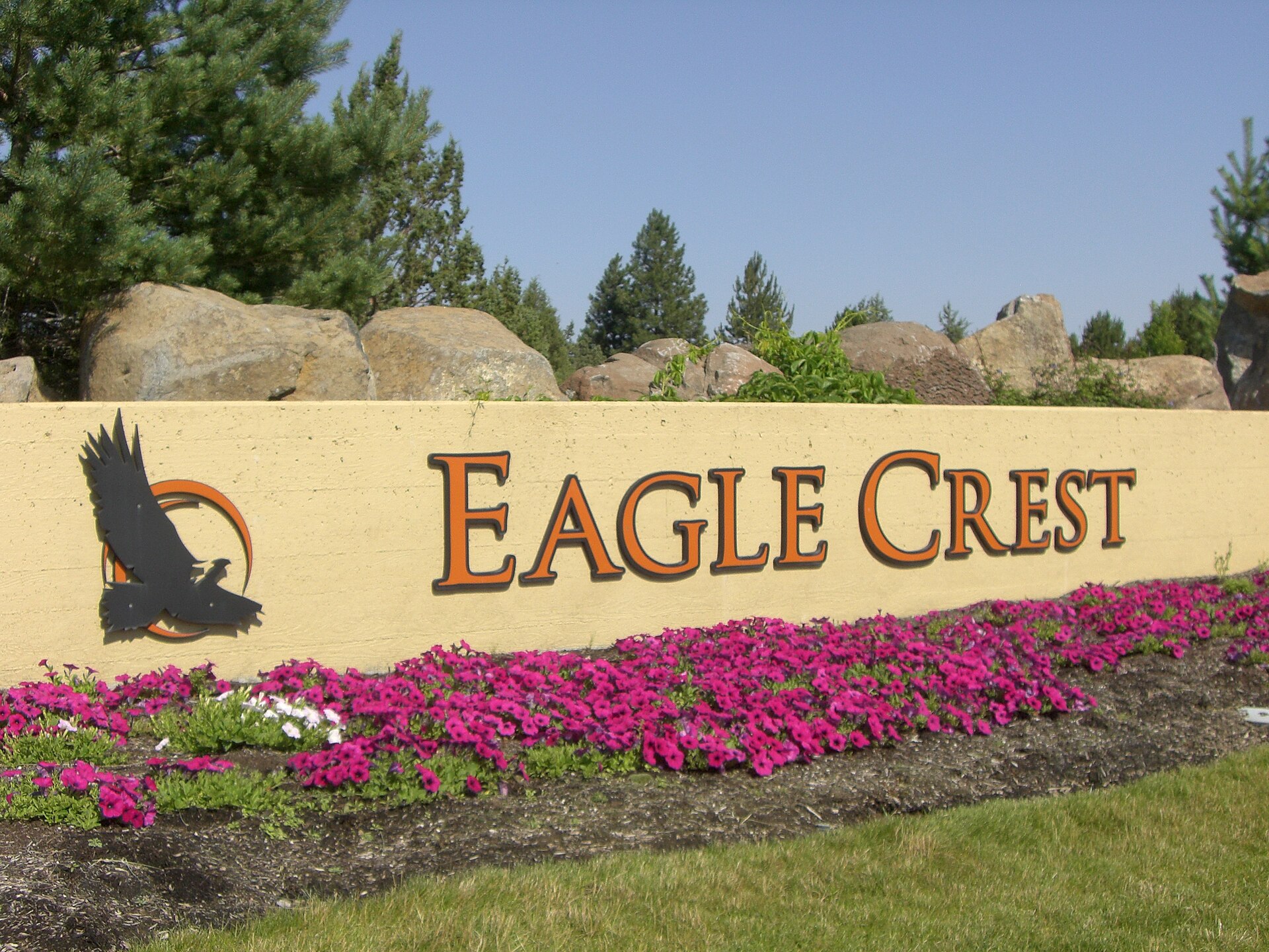 "Eagle Crest" entrance sign with an eagle emblem above pink flowers