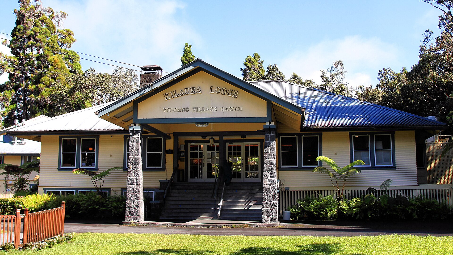 A low yellow lodge building with a covered porch and stone pillars, surrounded by trees in Volcano, Hawaii.