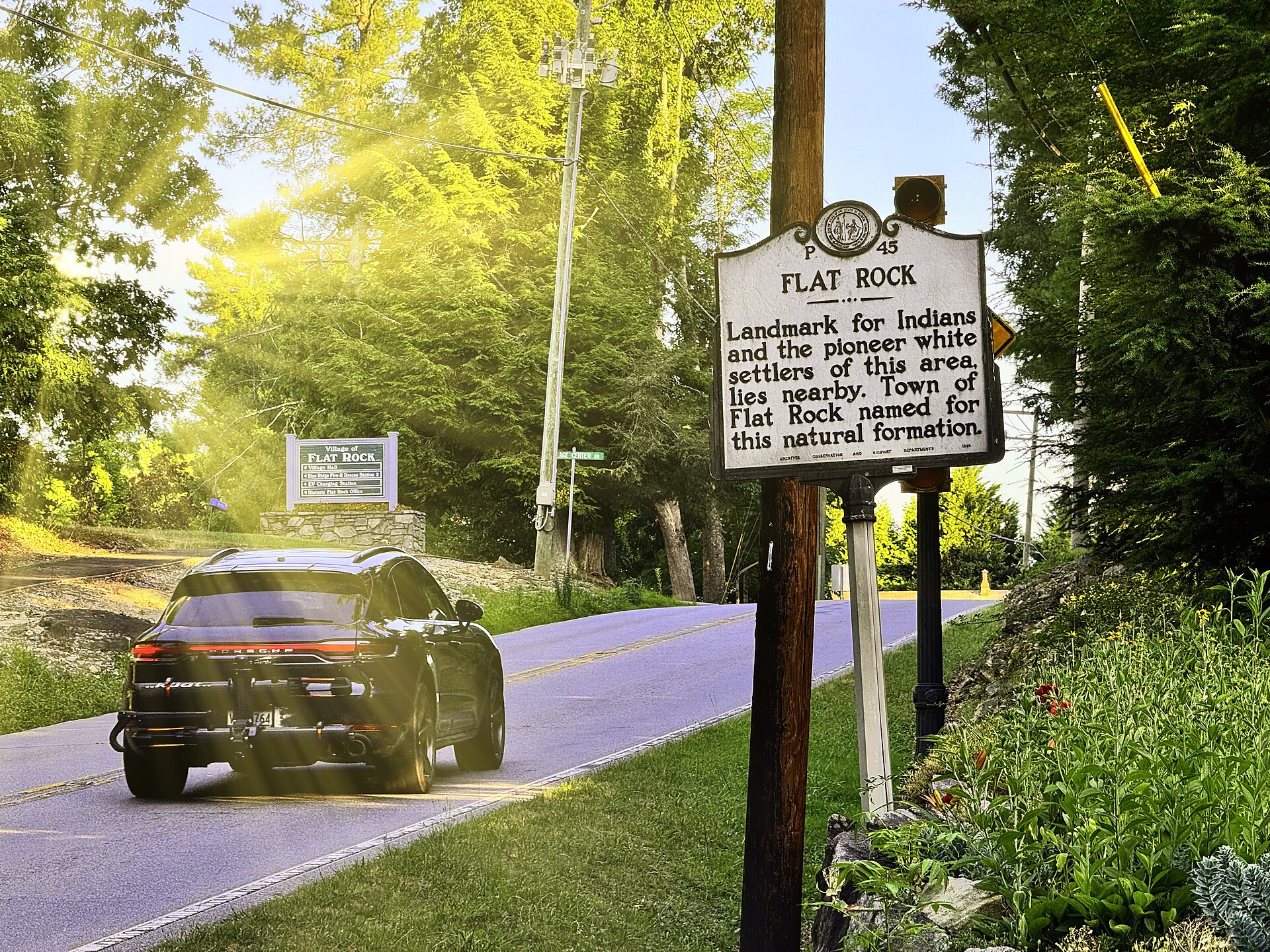 Historic marker reading "Flat Rock" beside a road, with a Village of Flat Rock welcome sign behind