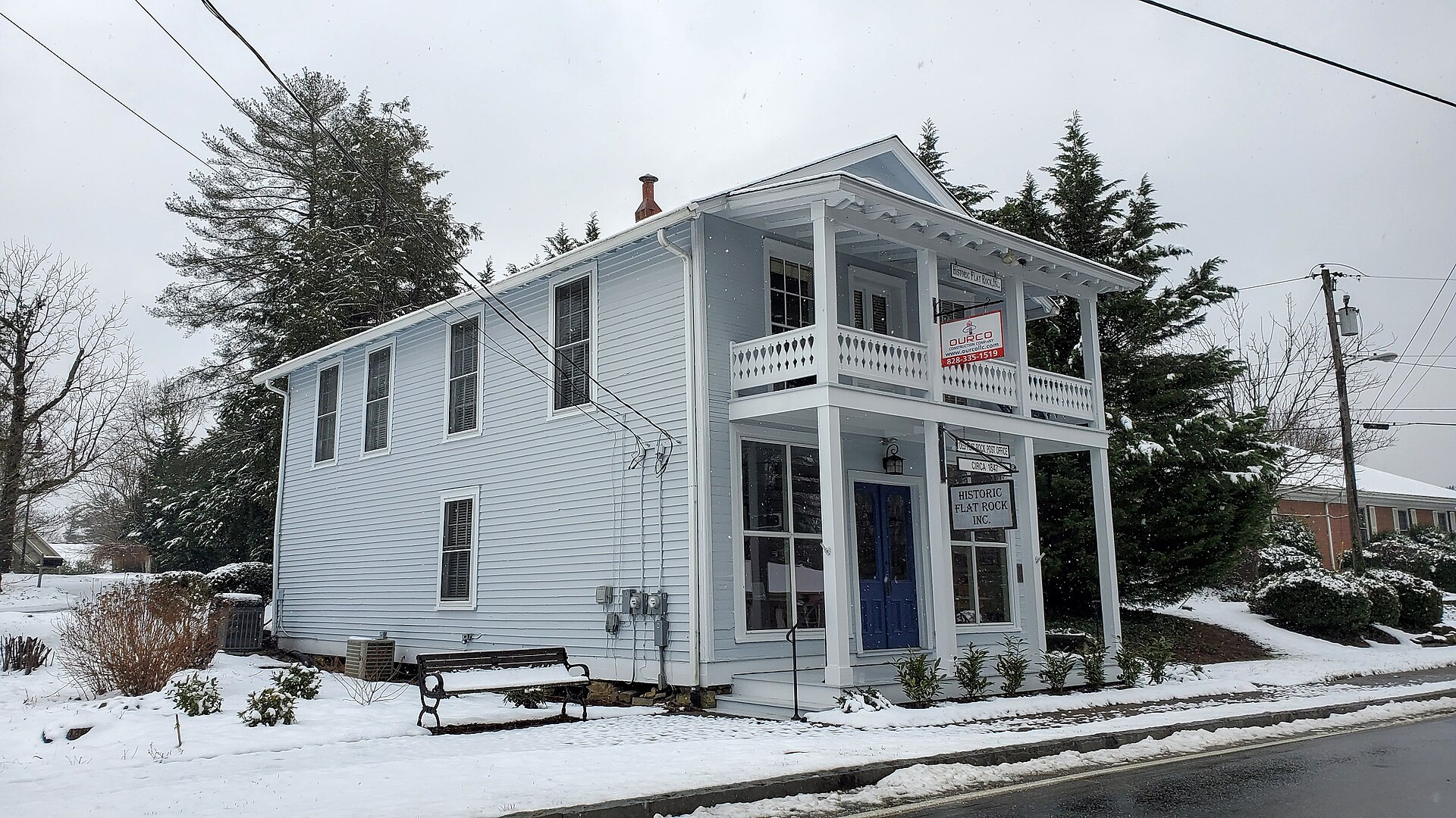 White two-story historic building with a "Historic Flat Rock Inc." sign, dusted with snow