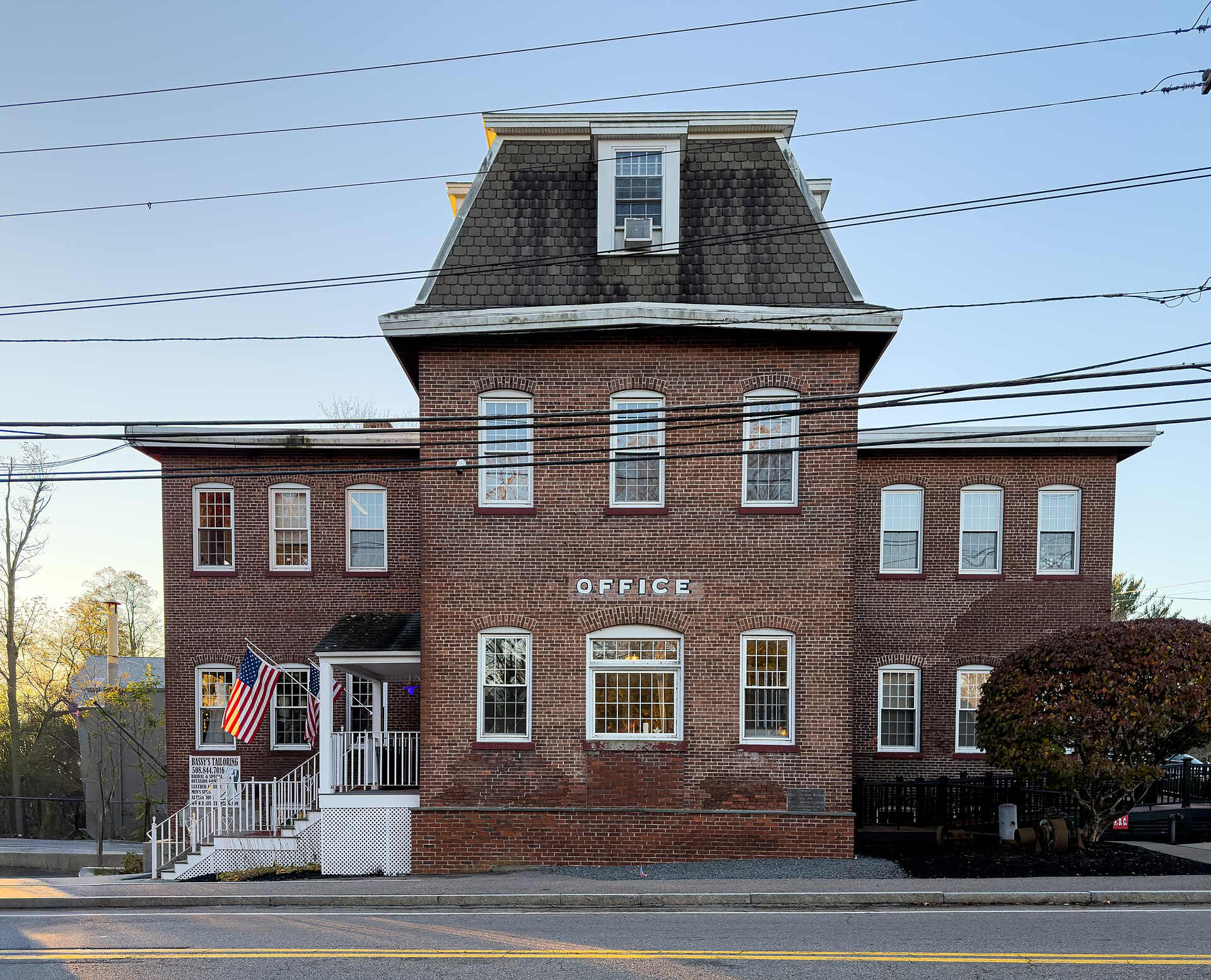 A historic red-brick former mill office building with American flags in Norton Center, Massachusetts