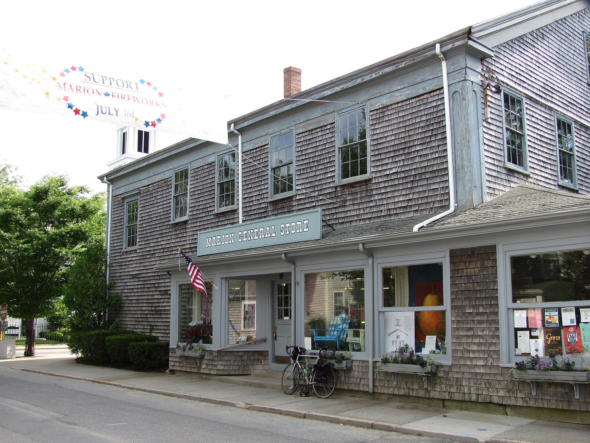 The shingled Marion General Store building with its sign, an American flag, and display windows in Marion, Massachusetts.