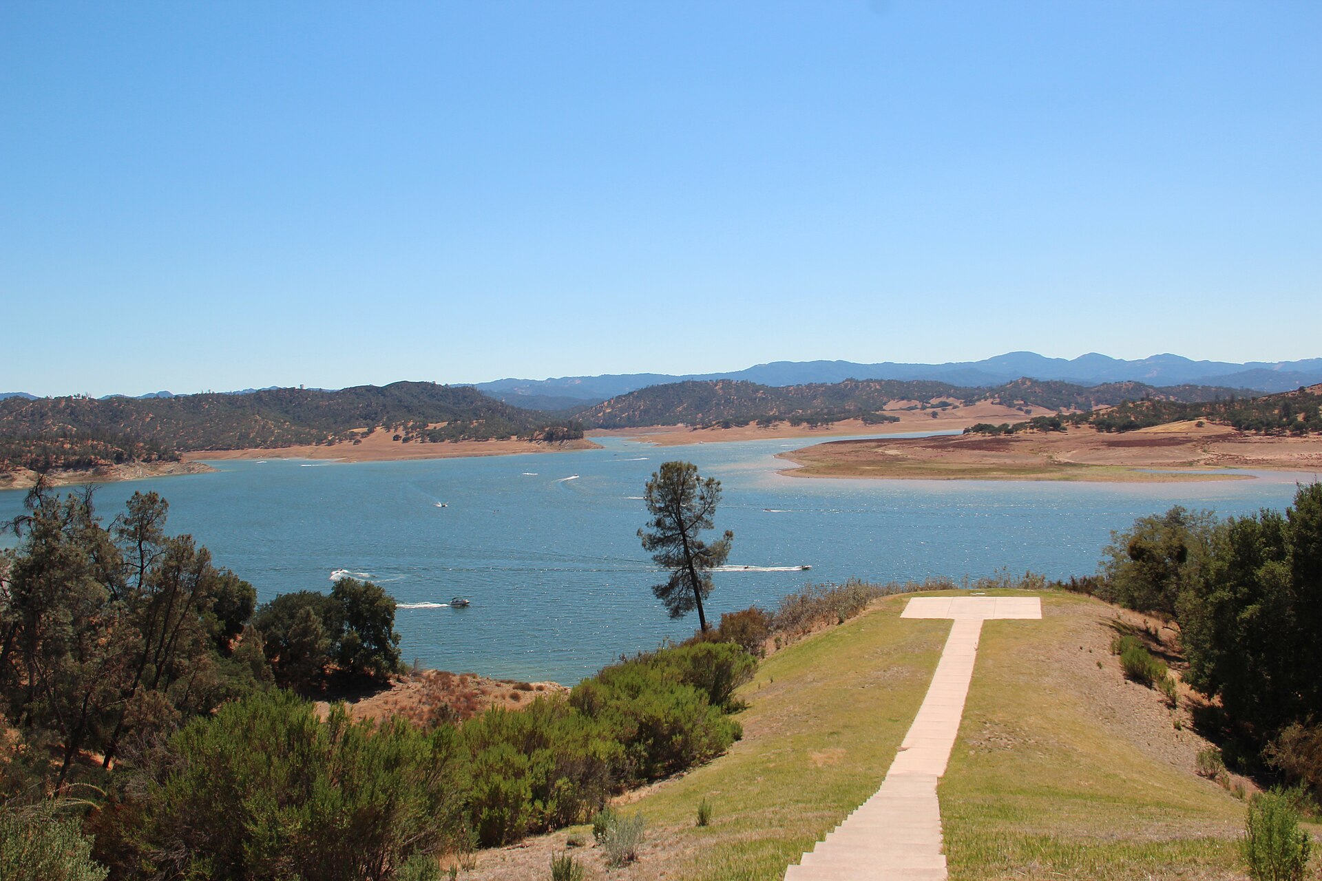 Lake Nacimiento with a walking path in the foreground and hazy hills across the blue water.