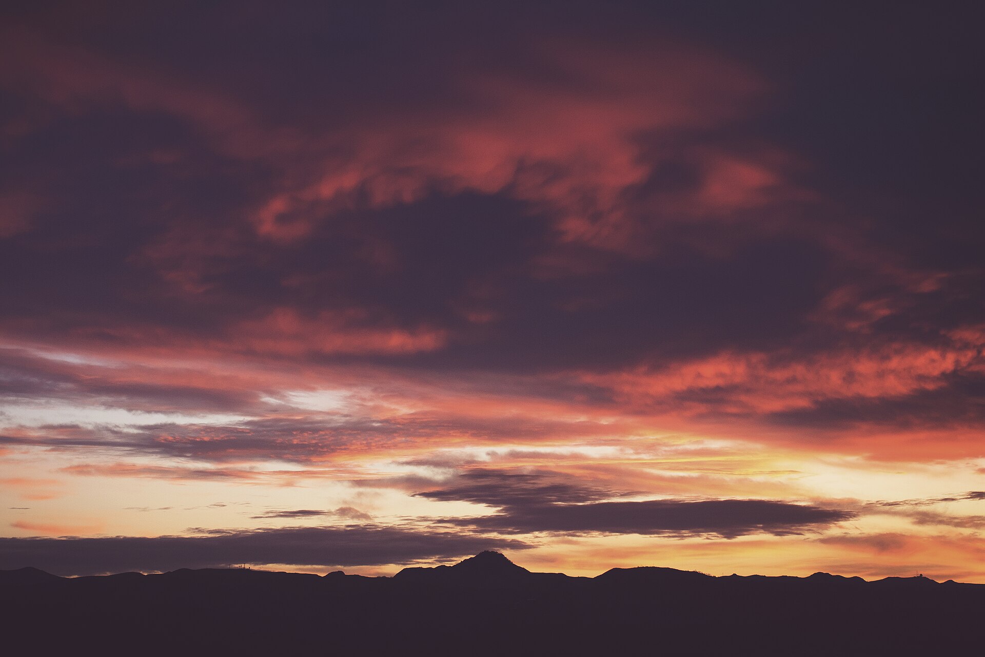 A colorful sunset sky with pink clouds over dark hills.