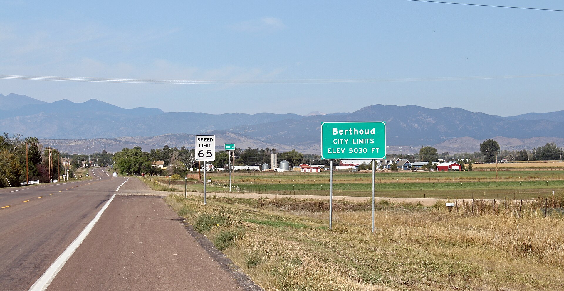 Green "Berthoud City Limits, elev 5030 ft" sign beside a road with foothills behind