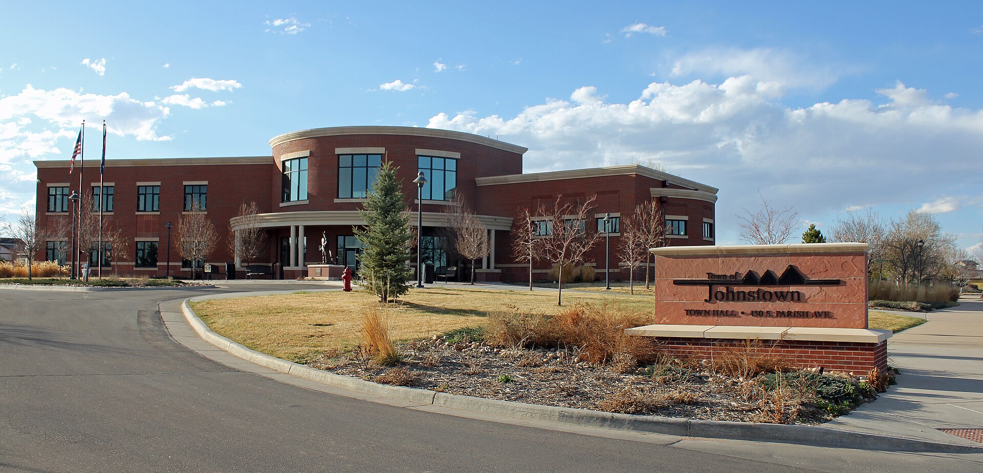 A brick town hall building with a curved entrance and landscaped grounds in Johnstown, Colorado.