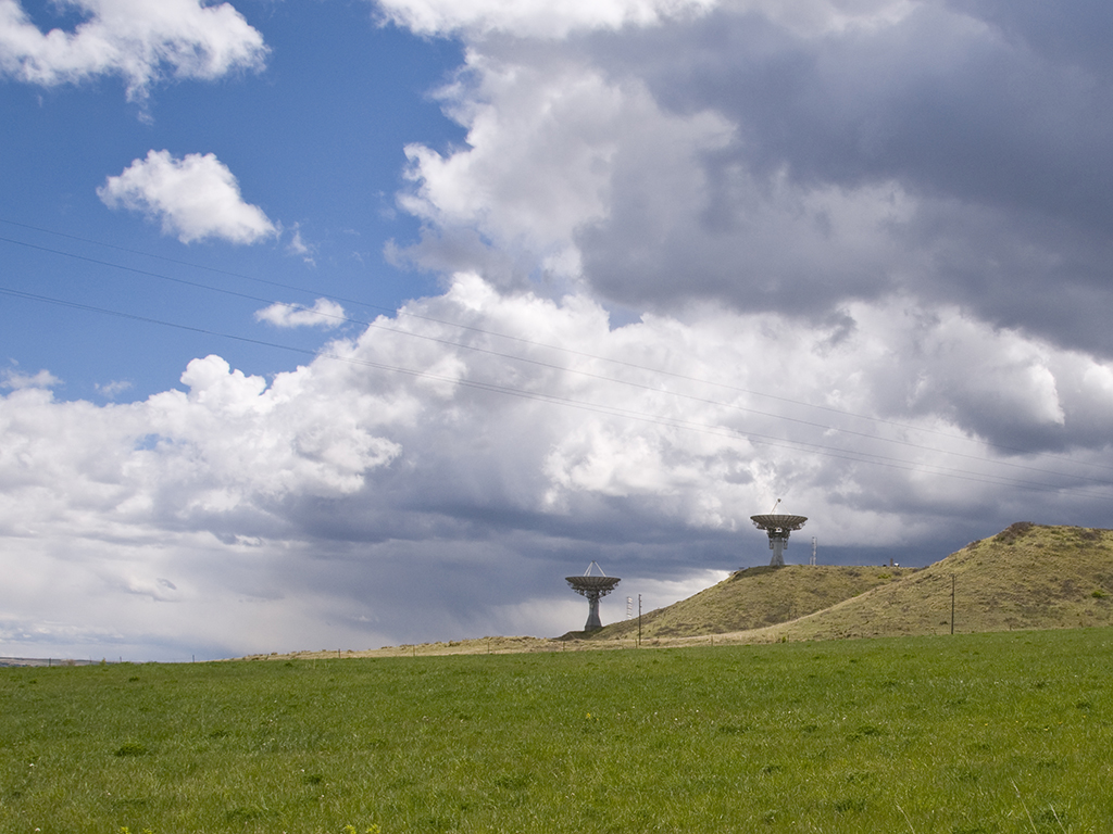 Satellite dishes on a grassy hill under a cloudy sky near Longmont
