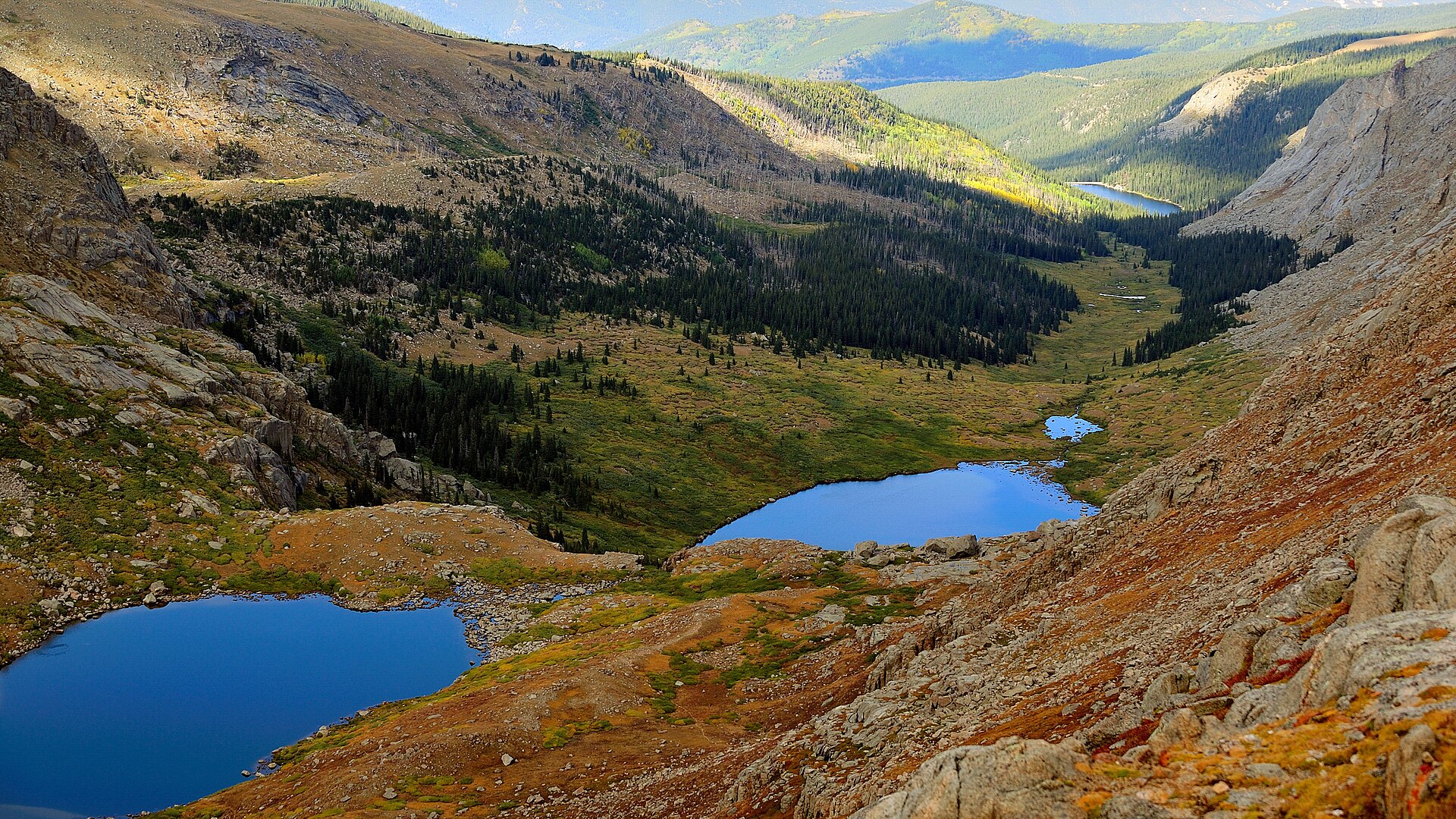 Two small vivid-blue alpine lakes nestled in a rocky high-mountain valley with autumn-tinted slopes.