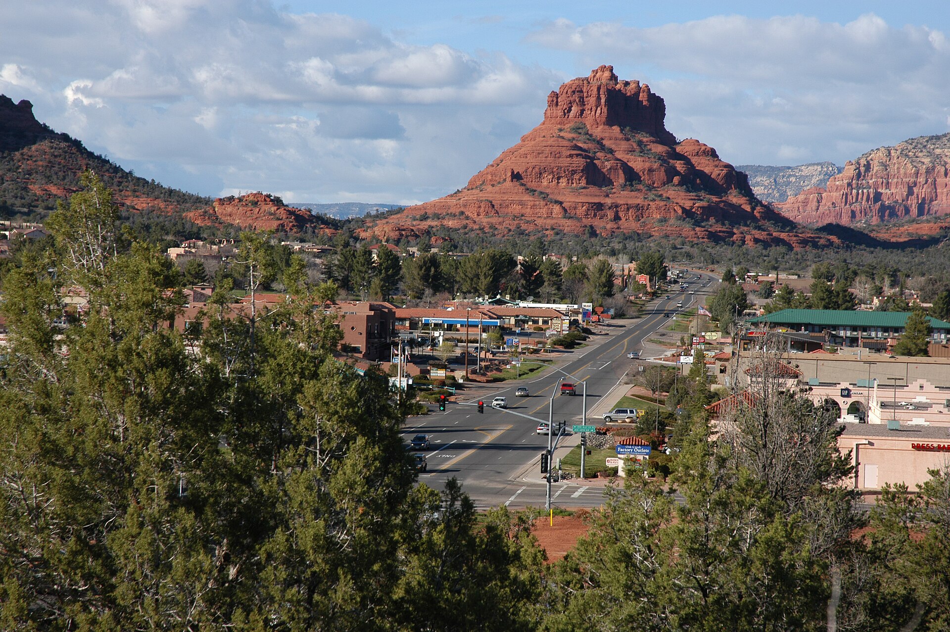 A town street with shops leading toward a red-rock butte under a blue sky.