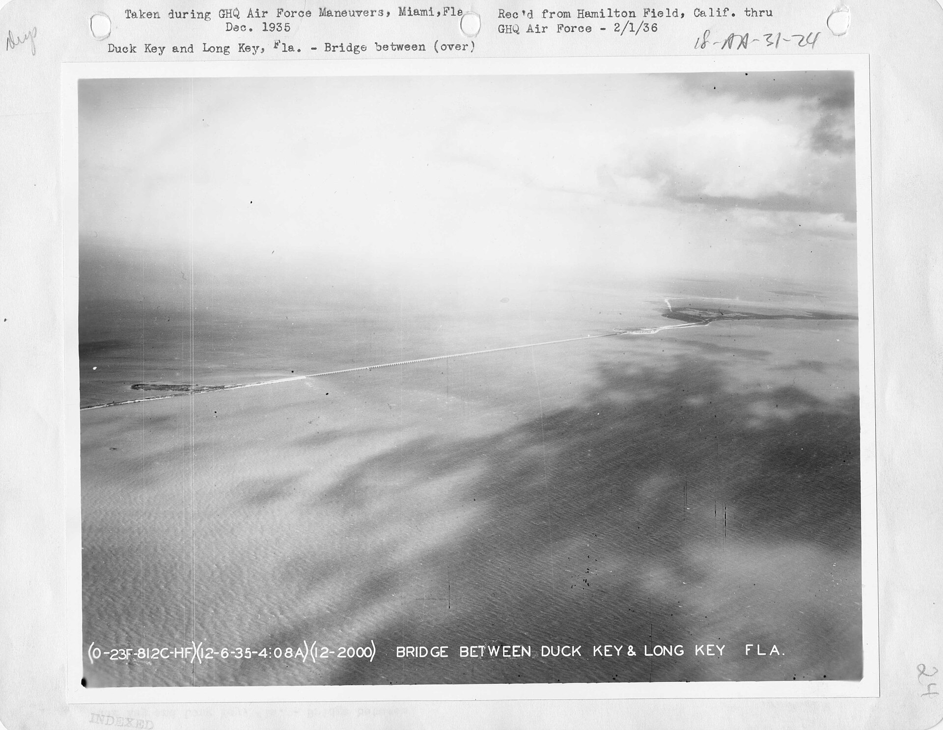 A black-and-white aerial photograph of a long bridge crossing shallow water between two low keys.