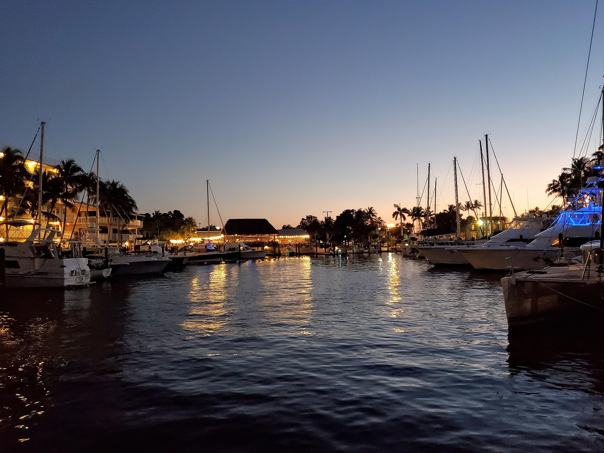 Boats docked at a Key Largo marina at sunset with lights reflecting on the water.