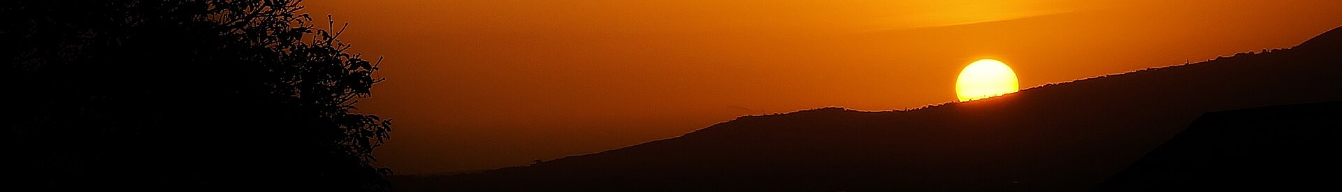 A panoramic orange sunset with the sun low over dark silhouetted hills.