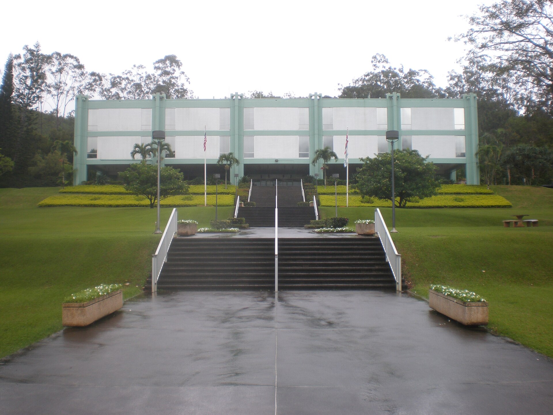 A modern mint-green academic building atop a grand staircase with lawns and planters in front.