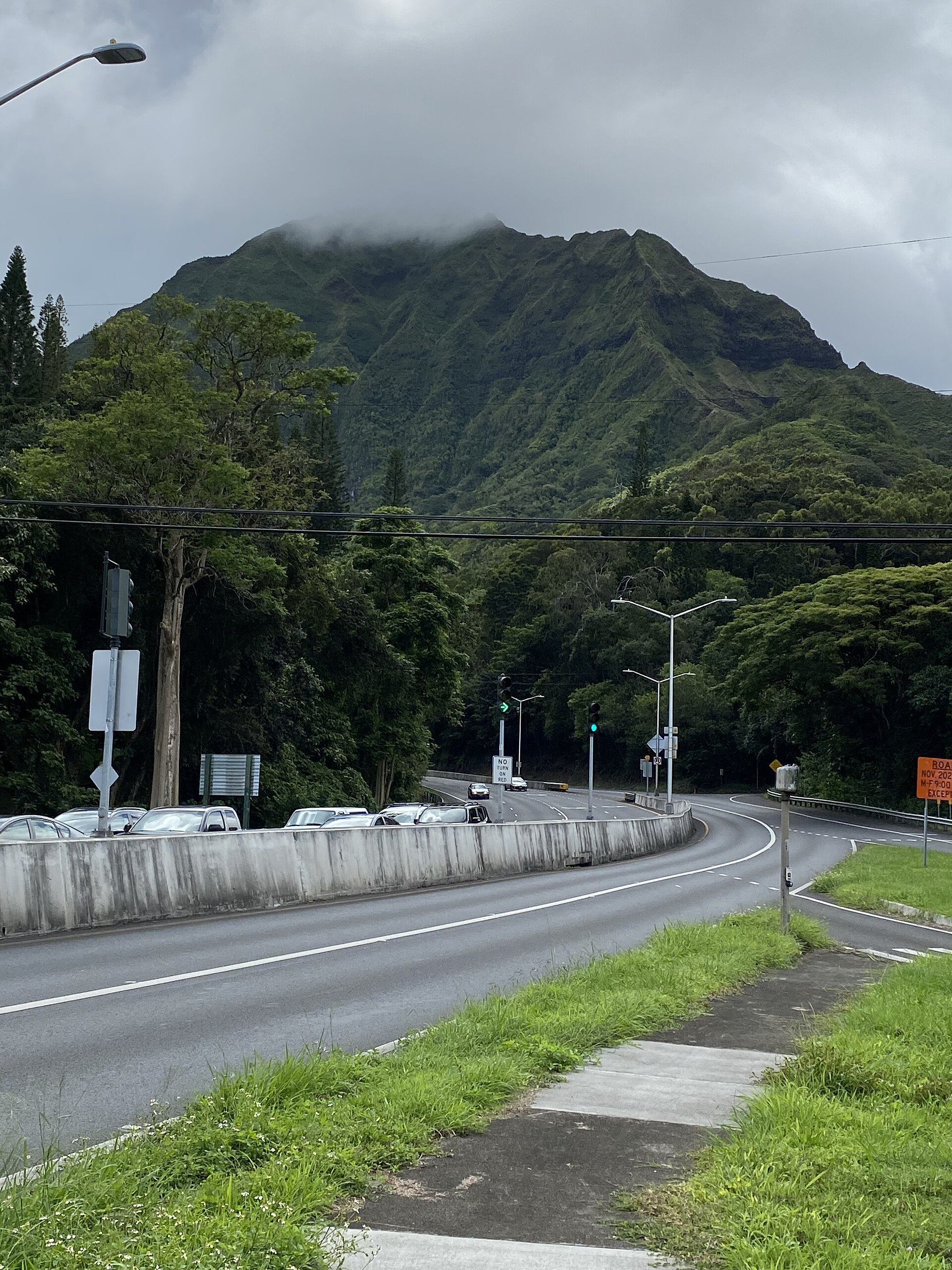 A curving highway with traffic beneath steep cloud-capped green mountains.