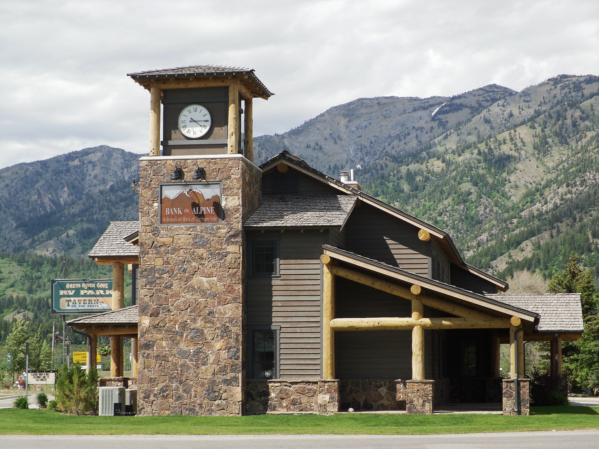 A stone and timber building with a clock tower in Alpine, Wyoming, backed by forested mountains.
