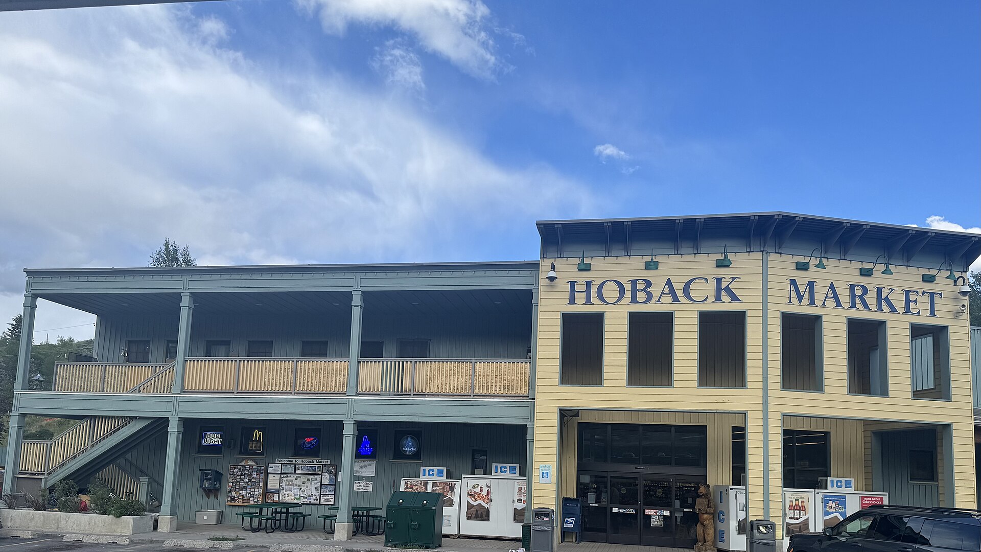 A two-story wooden general store with a 'HOBACK MARKET' sign, balconies, and storefronts under a blue sky.