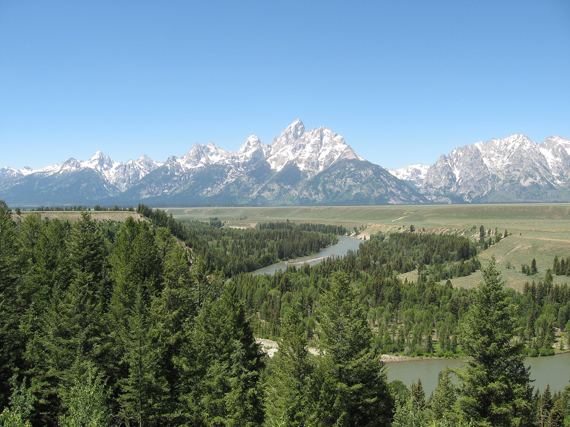 Snow-capped Teton peaks rising above evergreen forest with the Snake River winding below.