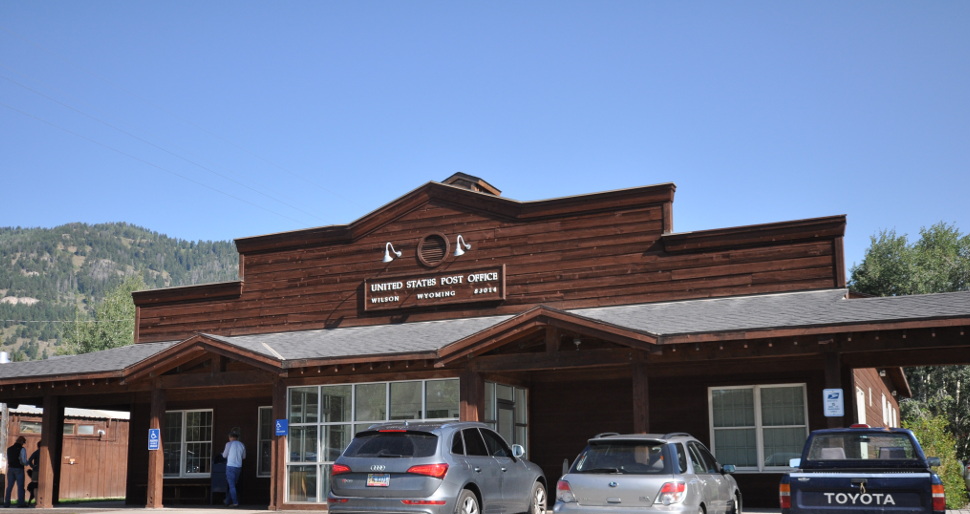 A small brown wooden post office building with a flagpole in Wilson.