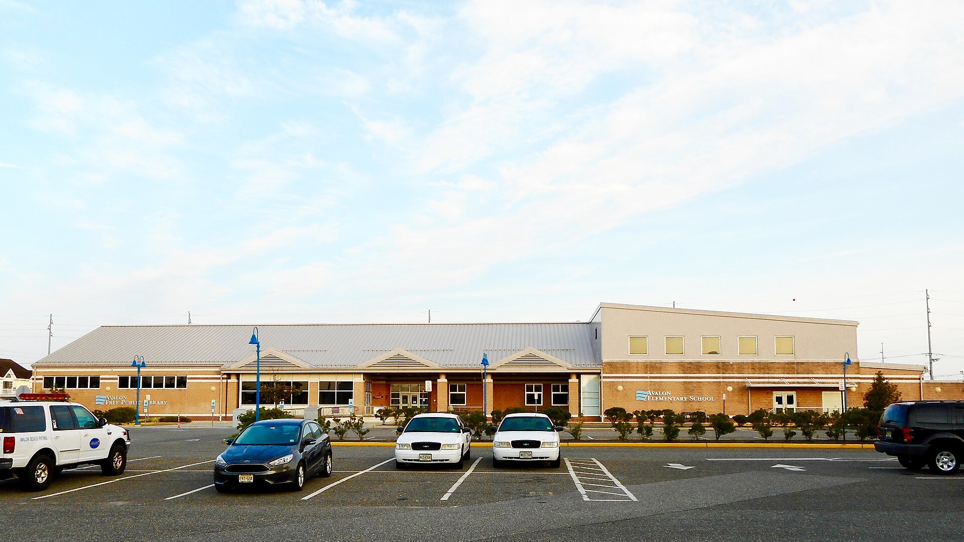A modern brick school and library building with a flagpole under a blue sky.