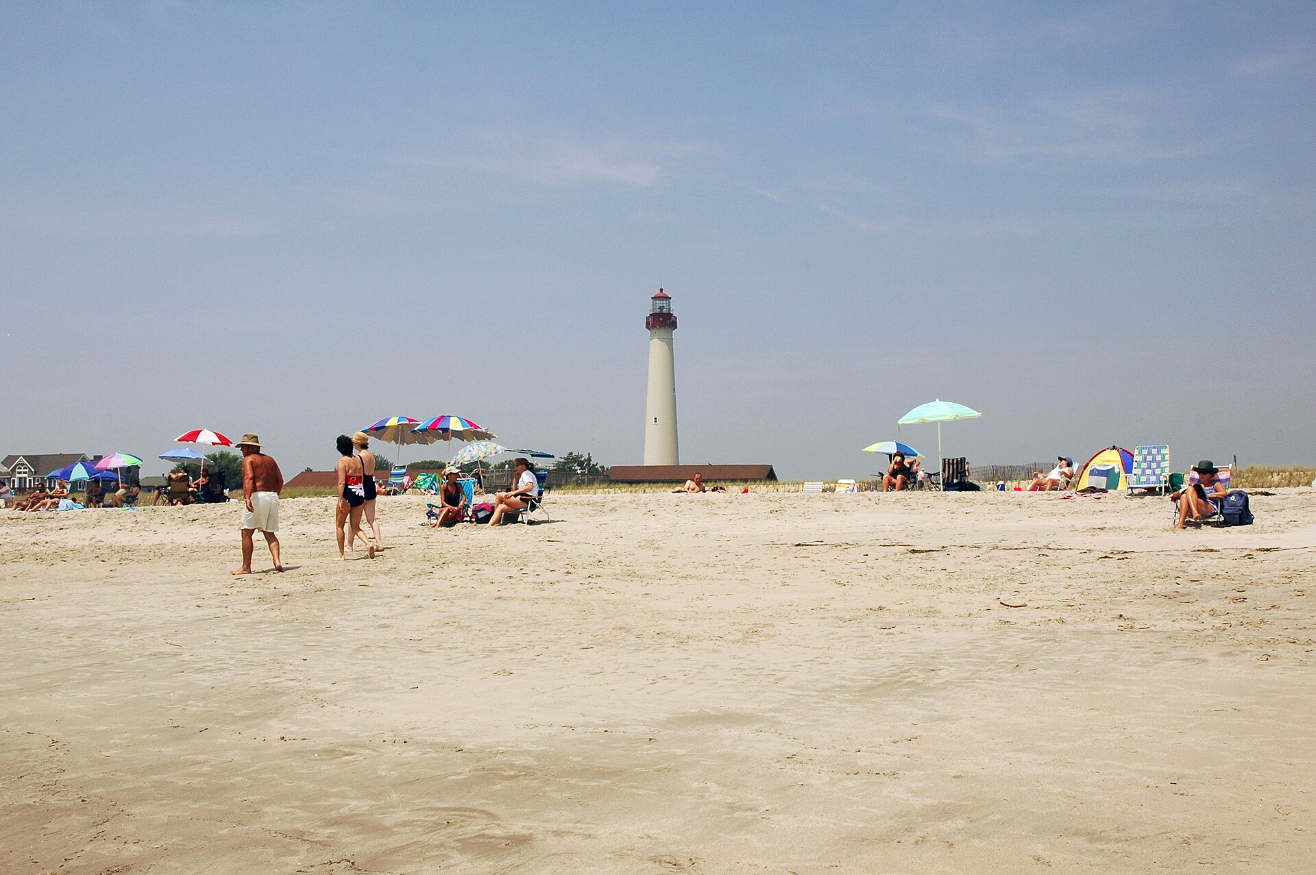 Beachgoers with colorful umbrellas on a wide sandy beach with the lighthouse in the distance.