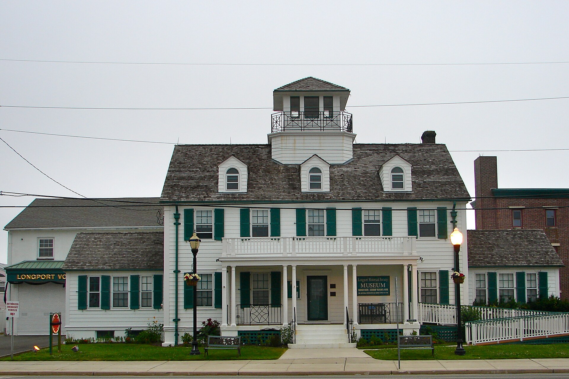 A white historic station house with green shutters, cupola, and wraparound porch.