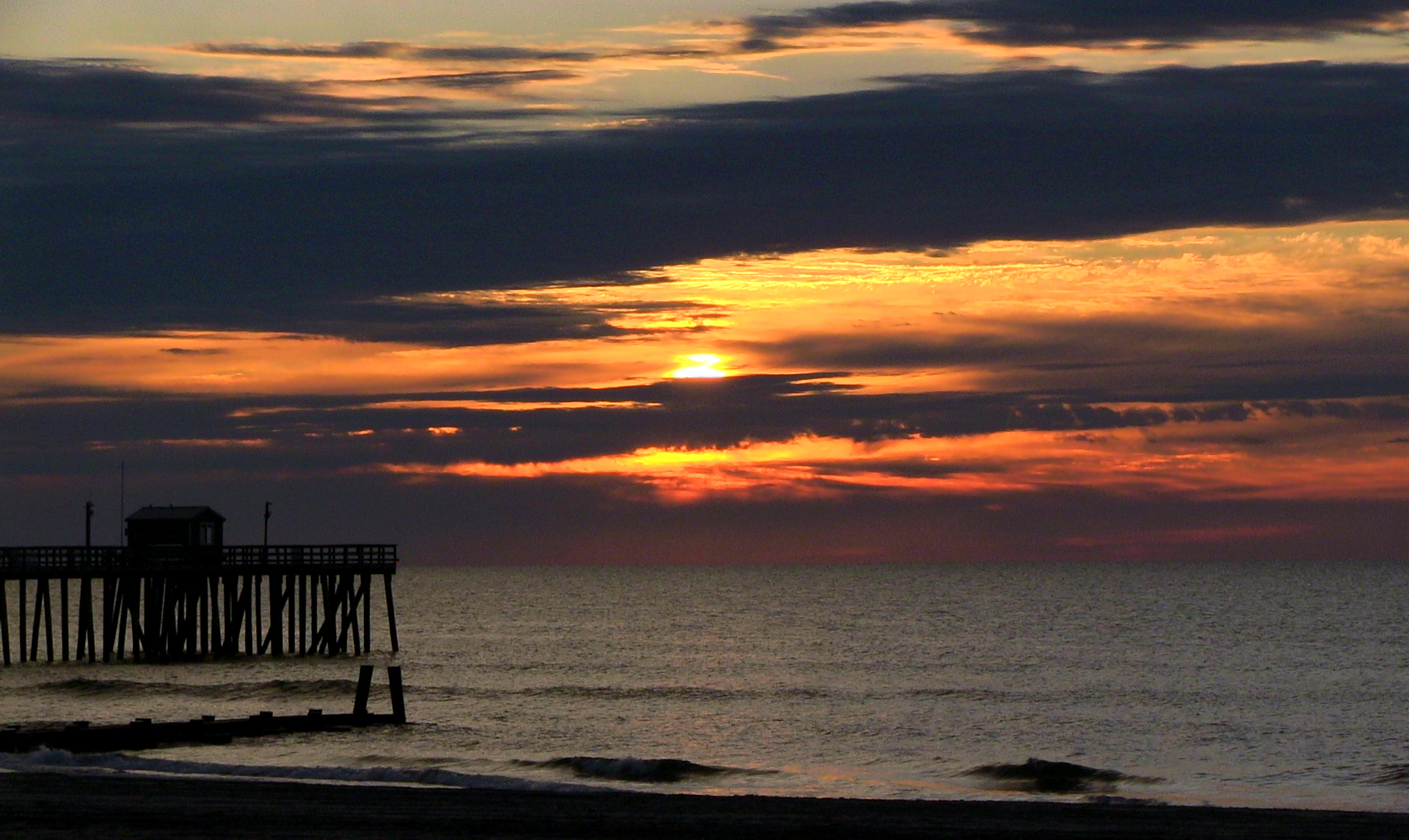 A sunrise over the ocean with a fishing pier in Margate City New Jersey.