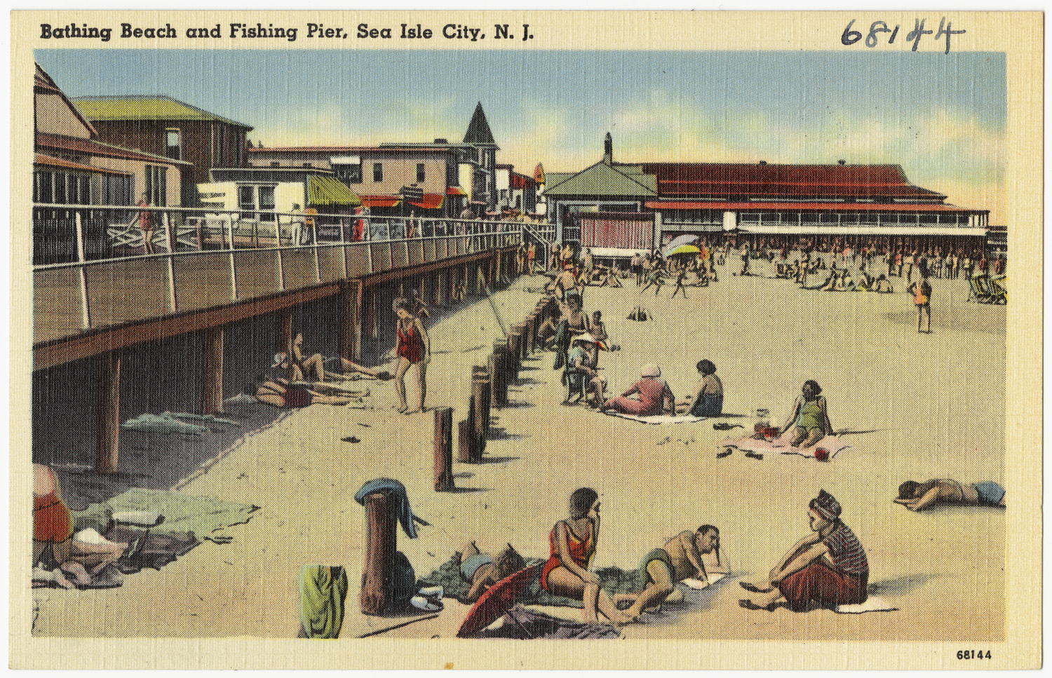 A hand-tinted vintage postcard of crowds on a sandy beach beside a long fishing pier with beachfront buildings.
