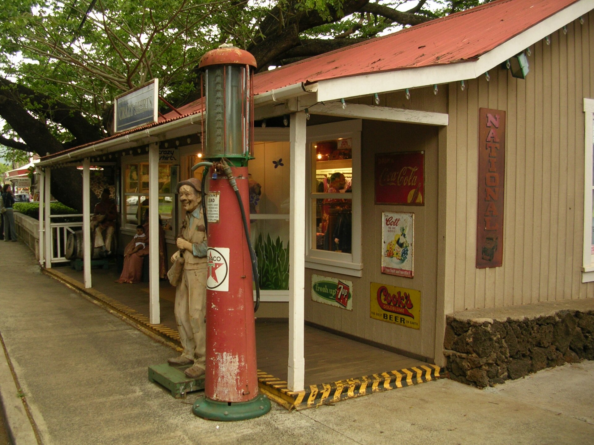 An old-fashioned general store with a red antique gas pump, wooden figure, and vintage Coca-Cola signs.