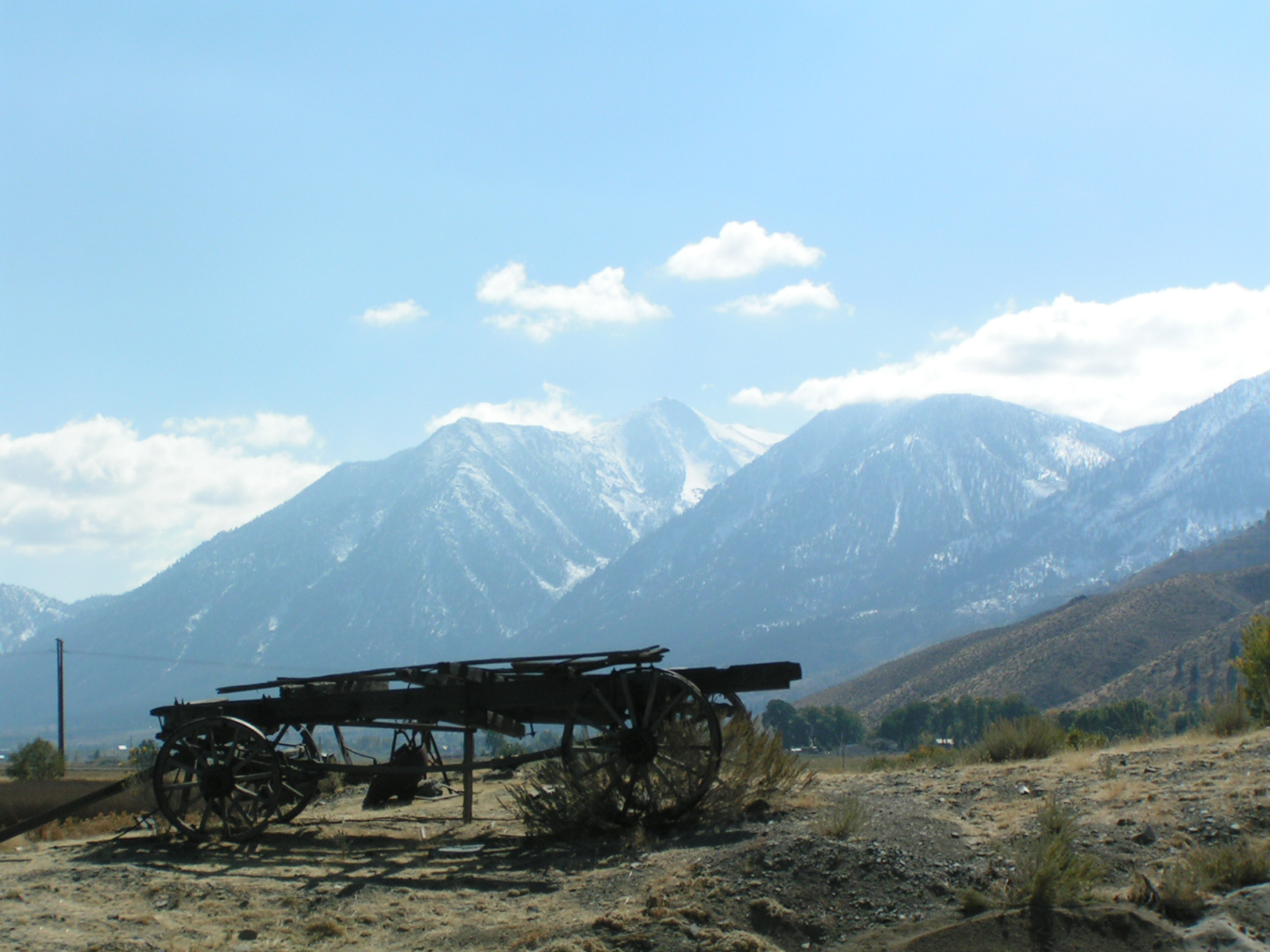 A weathered wooden wagon on a dirt field with the snow-dusted Carson Range rising behind.