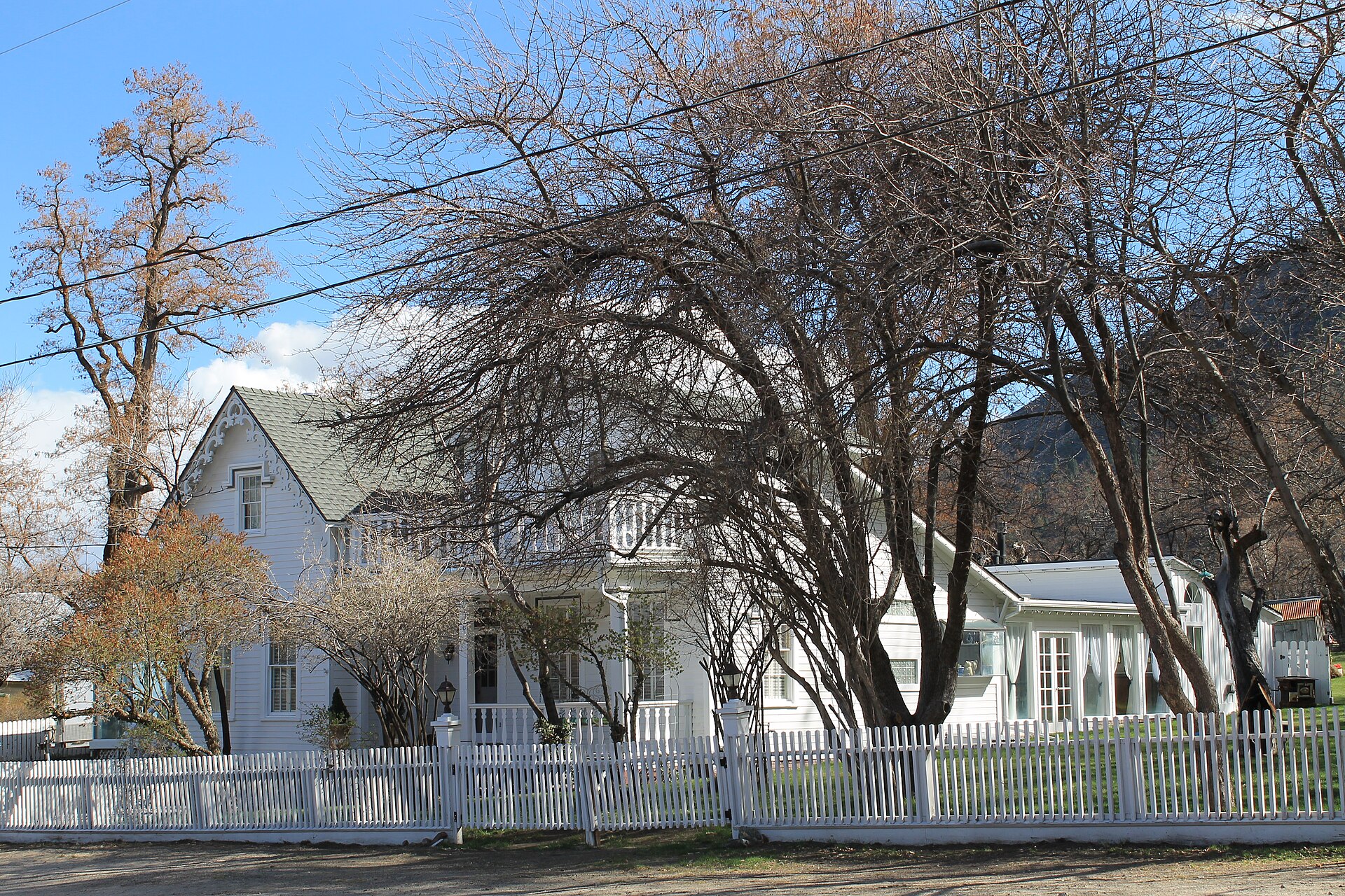 A white historic house with a picket fence and bare winter trees under a blue sky.