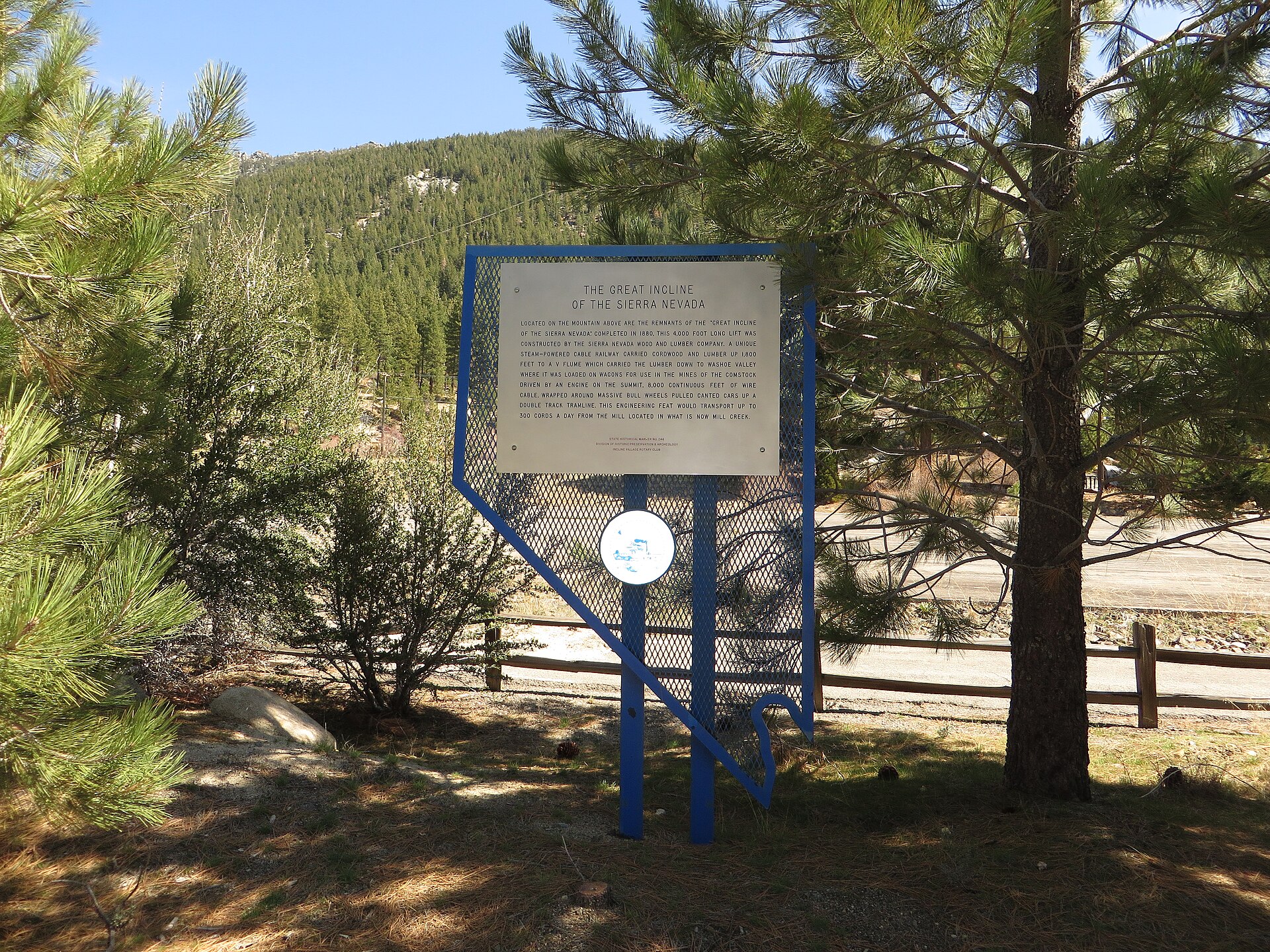 A Nevada historical marker with mountain scars visible on the forested slope above.