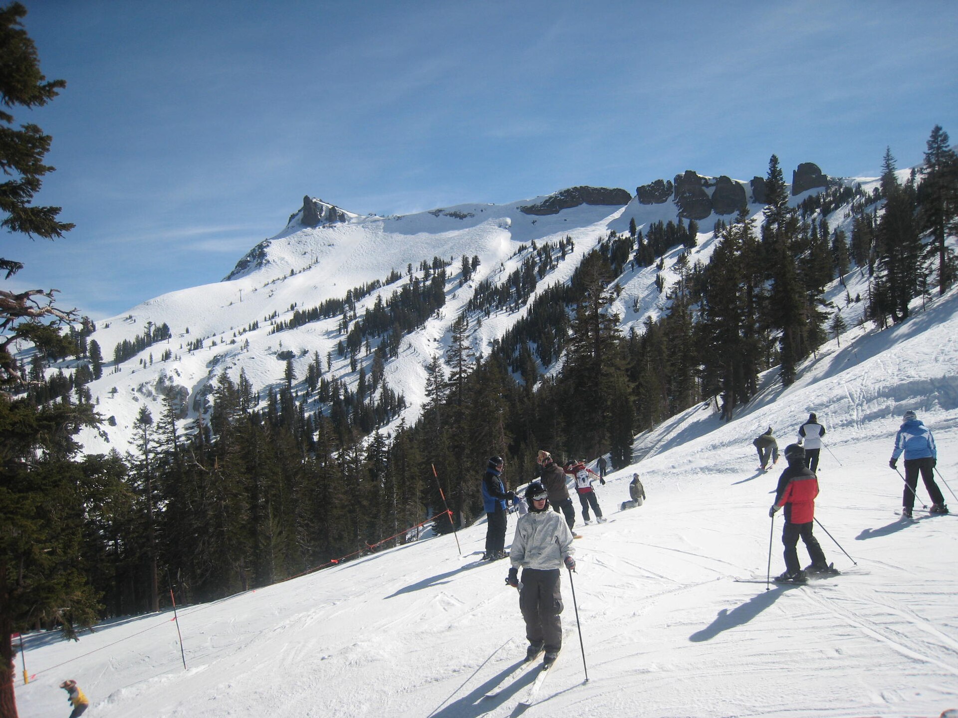 Skiers riding up and down a snowy slope at Kirkwood Mountain Resort with pine trees.