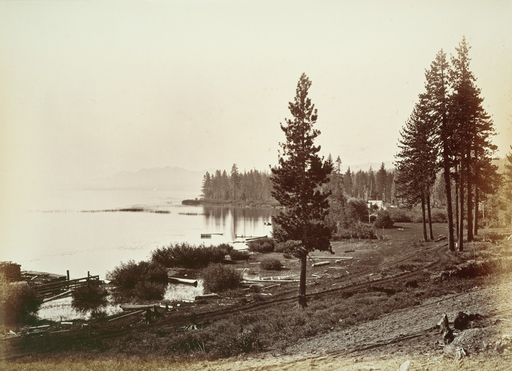 A sepia 19th-century view of the lake shoreline with pines, a pier, and distant mountains.