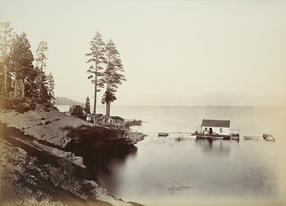 A sepia 19th-century view of a small boathouse on calm water beside a rocky pine-covered point.
