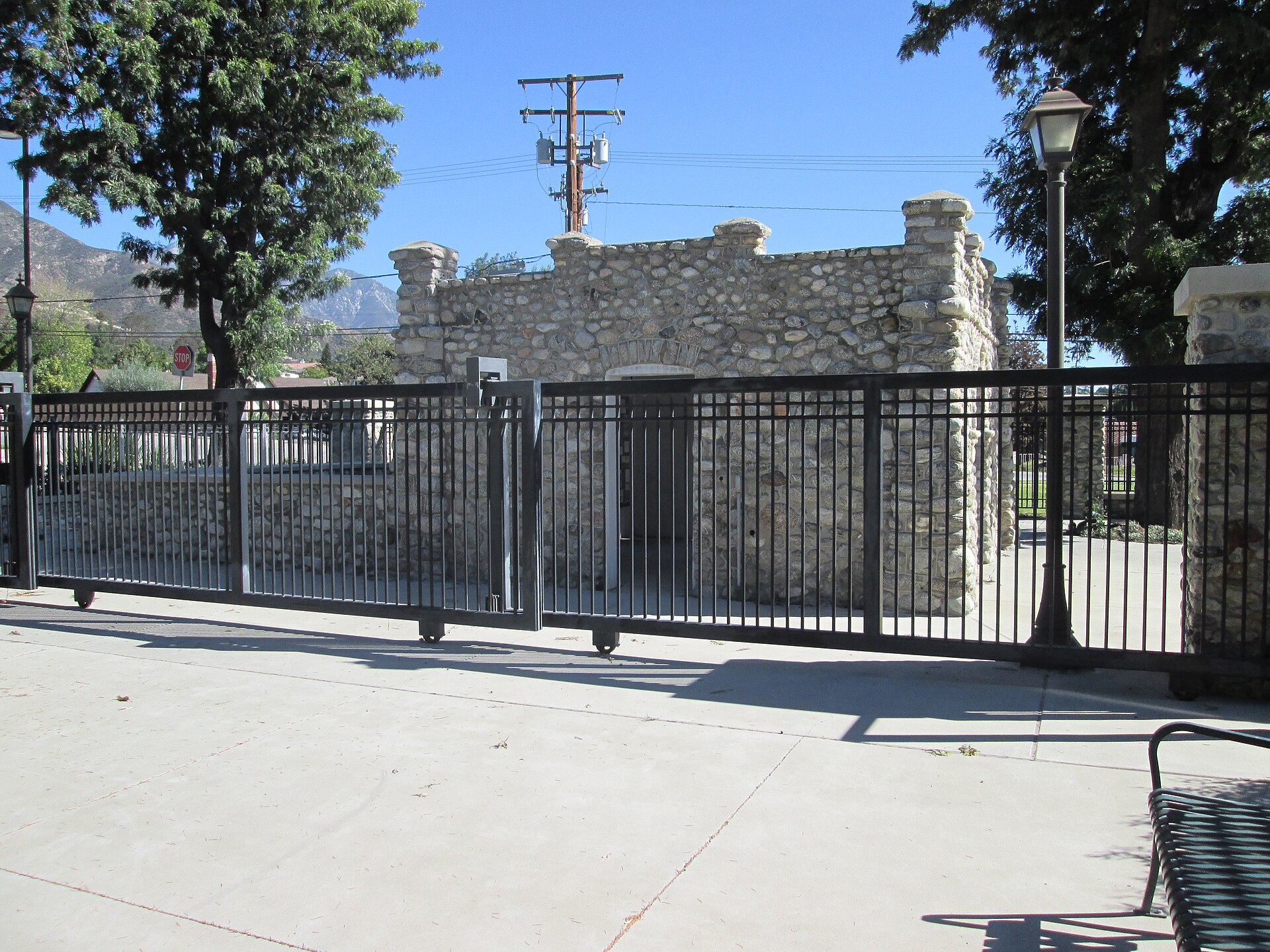 A small historic stone streetcar station behind an iron fence, with mountains behind.
