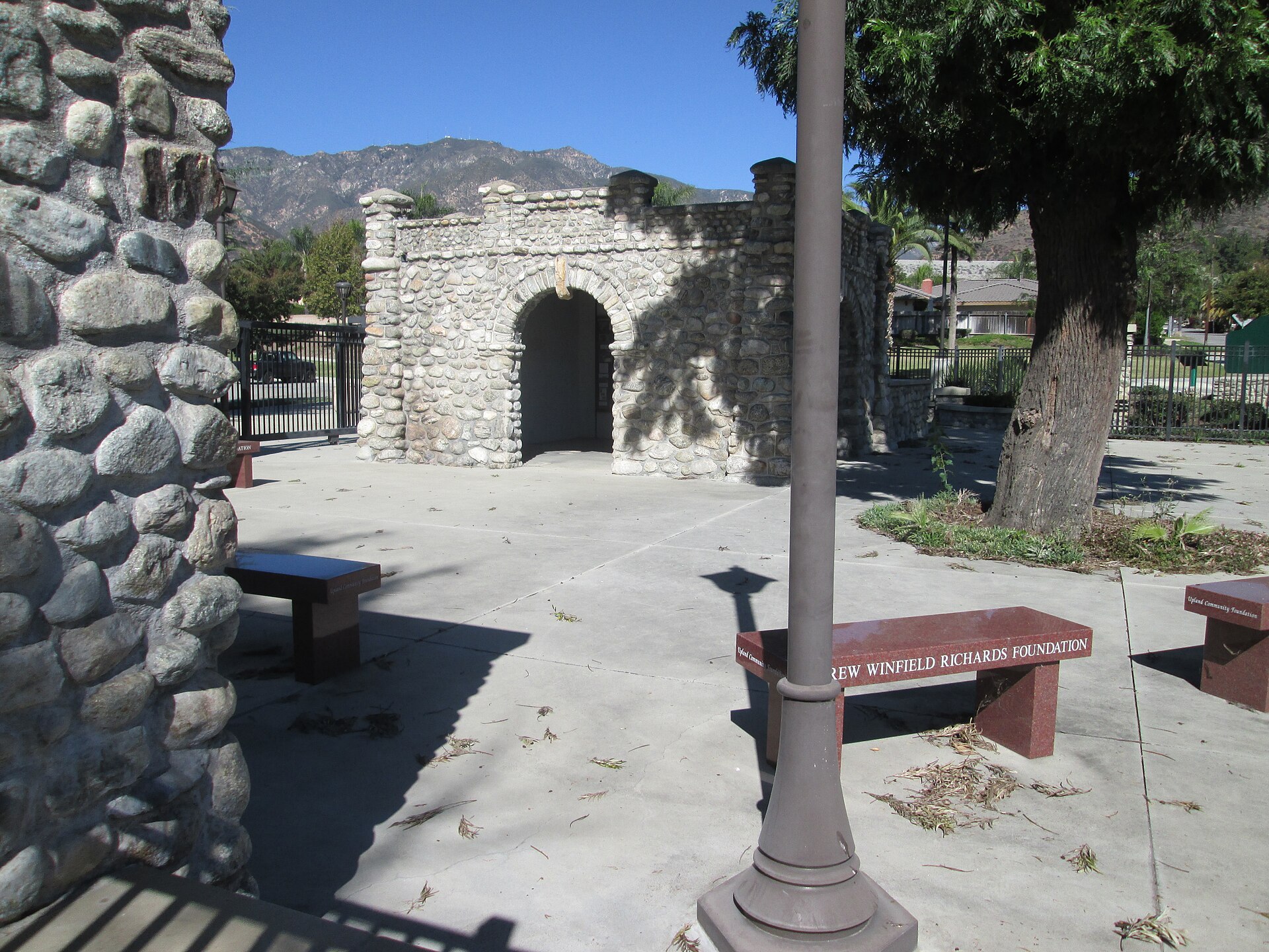 A stone archway station with benches and a memorial plaque, backed by mountain ridges.