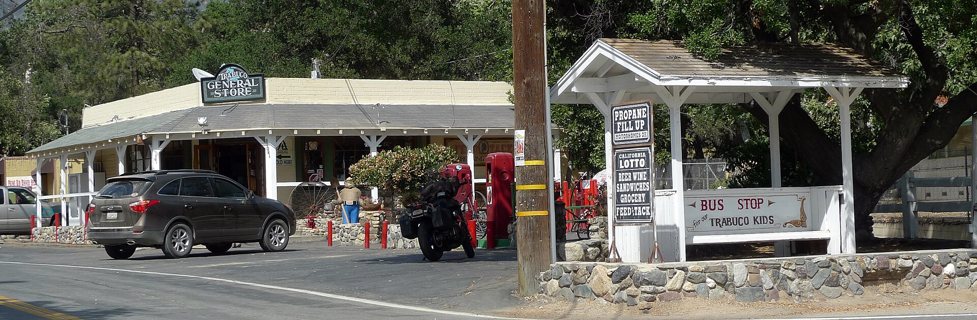 A rustic general store with a covered porch, signs, and a small bus shelter across the road.