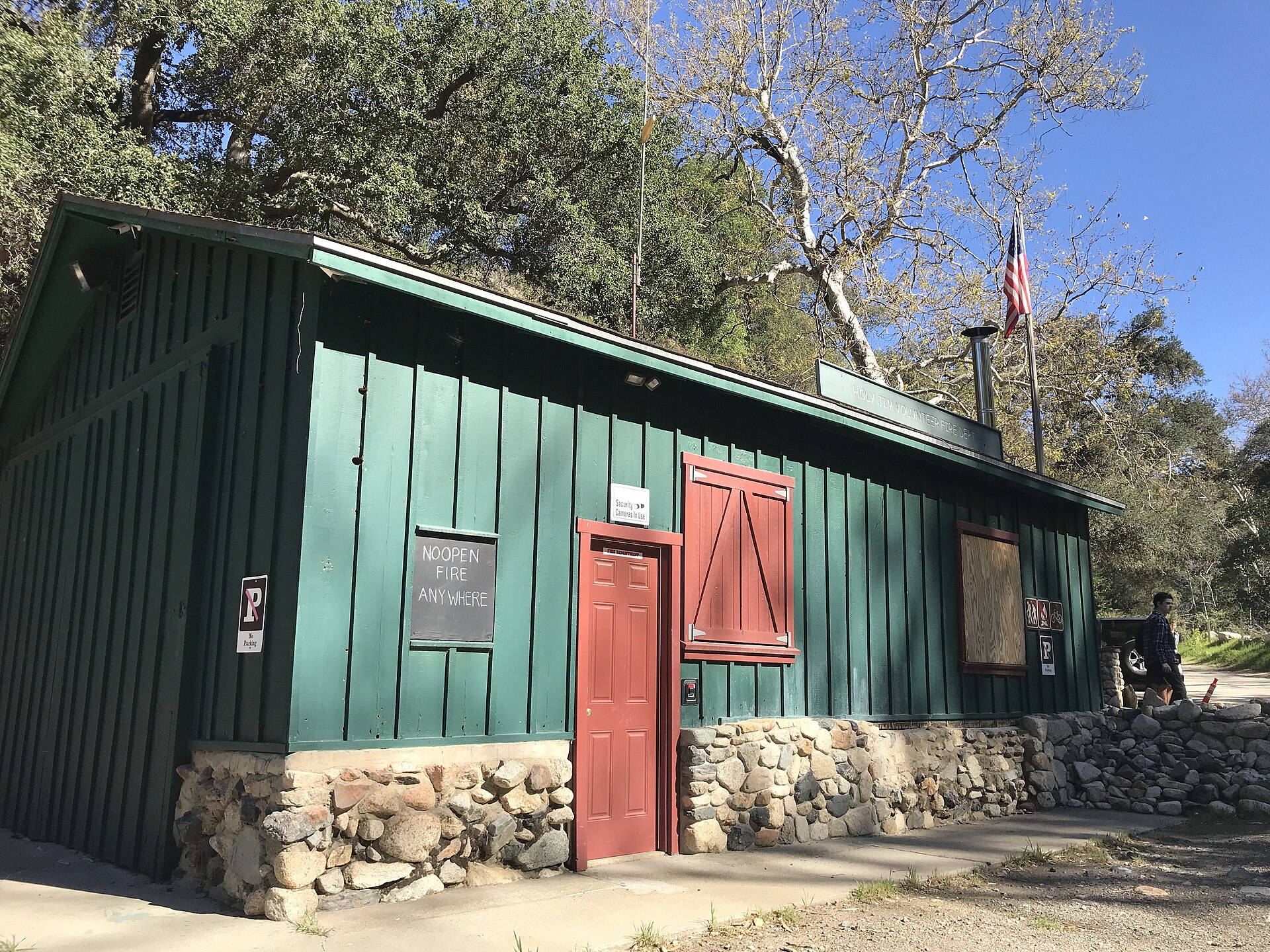 A rustic green wooden fire station with a stone foundation and an American flag.