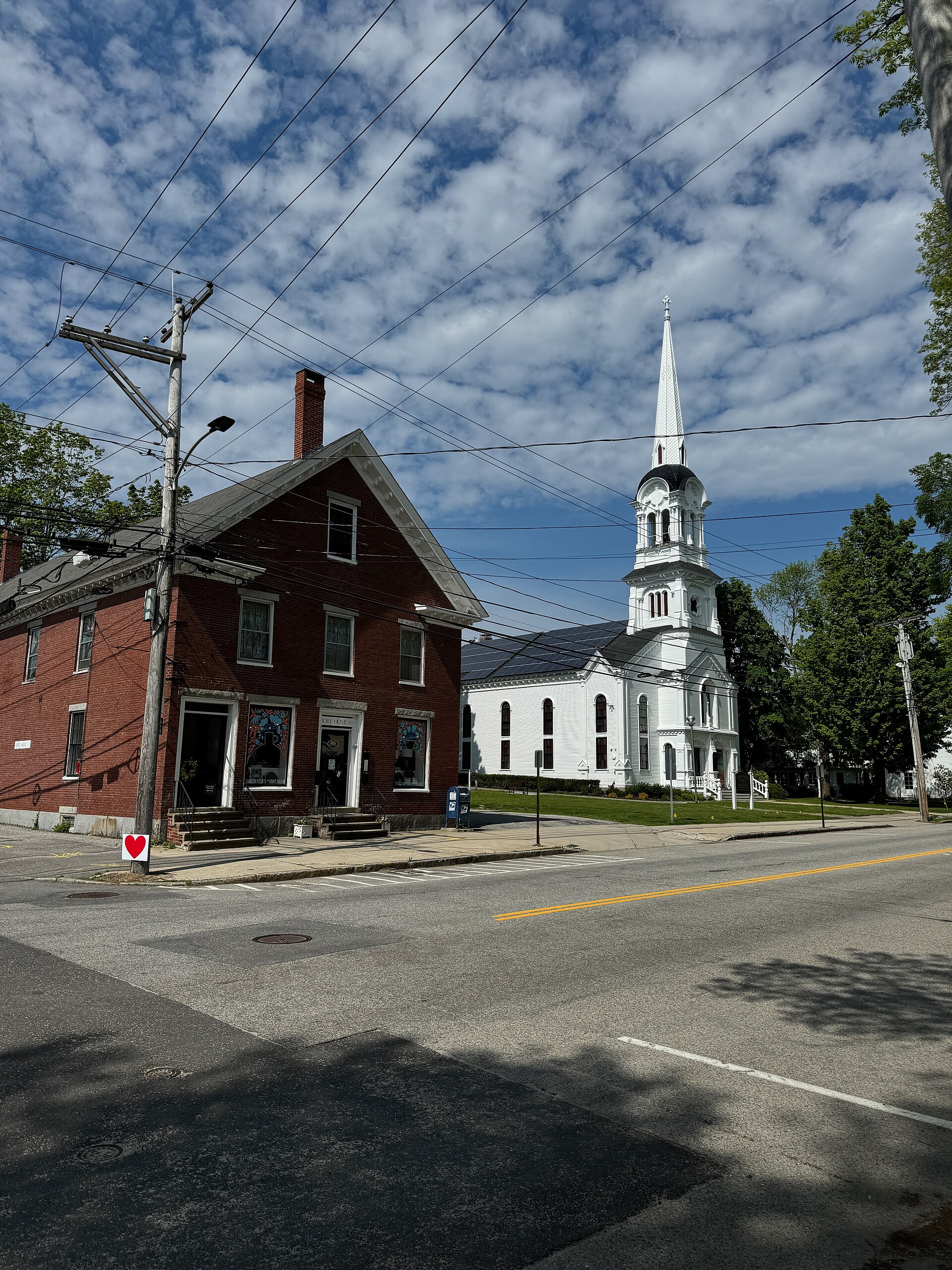 A brick commercial building at 108 Main Street in Yarmouth, Maine, next to a white church with a tall steeple.