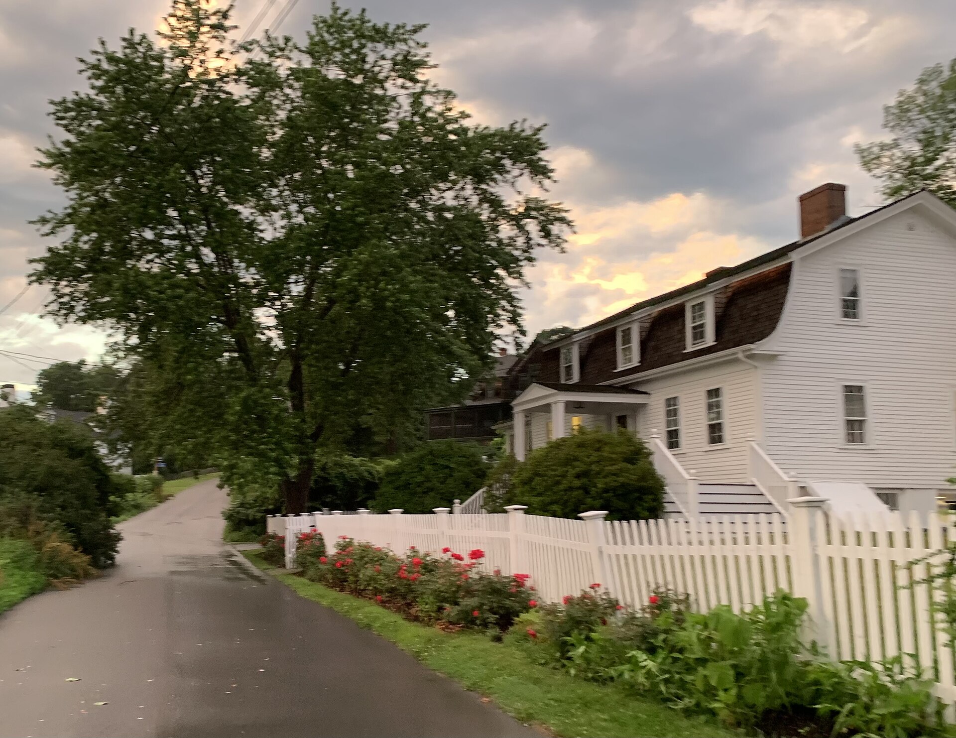 A historic white 1682 Dutch gambrel-roofed house behind a picket fence with red roses in York Harbor, Maine