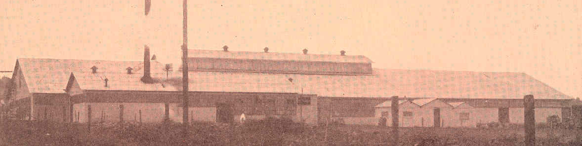 A sepia-toned historic photo of a long plantation-era industrial building with a fence in front.