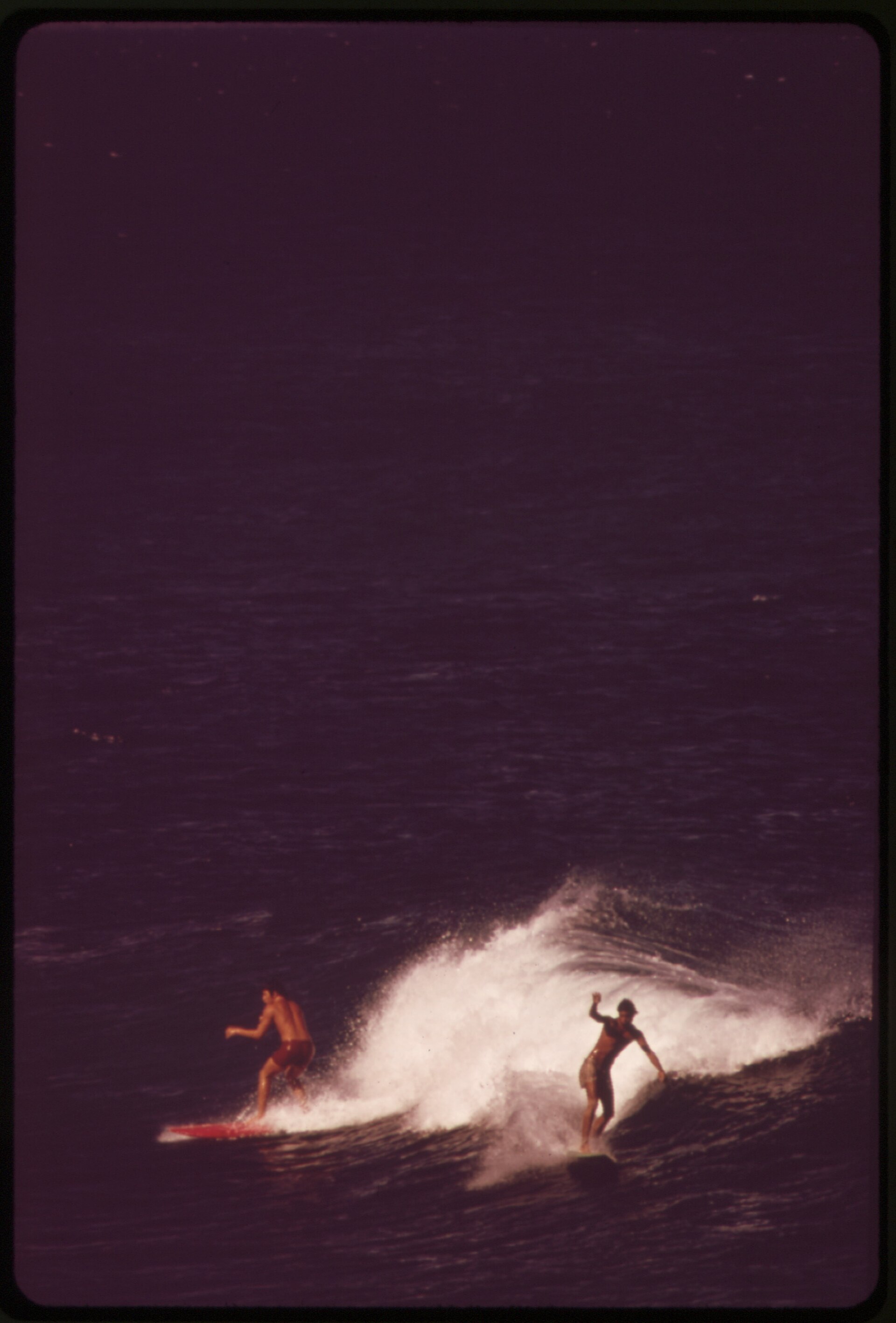 Two surfers riding a breaking wave in a vintage color photograph.