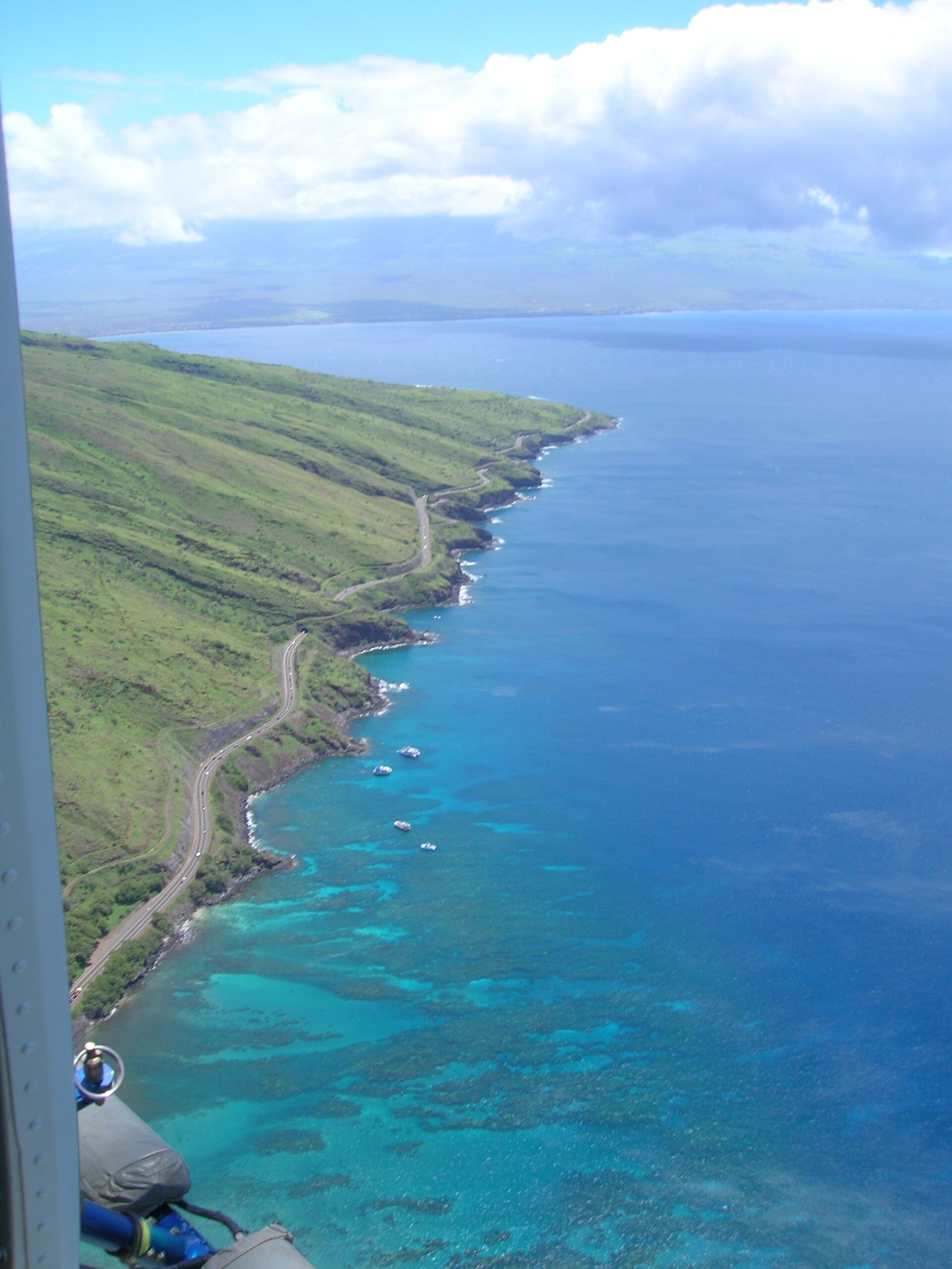 The coastal highway winding along green hills above turquoise water with boats anchored offshore.