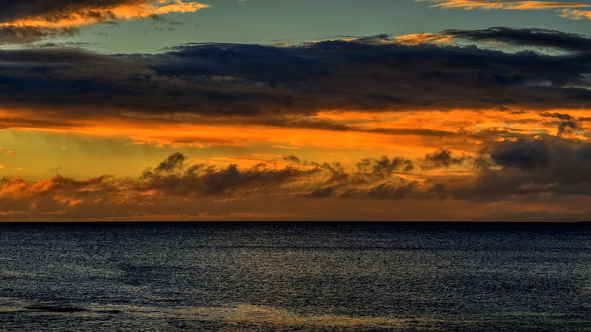 Fiery orange and gold clouds over a dark ocean at sunset.