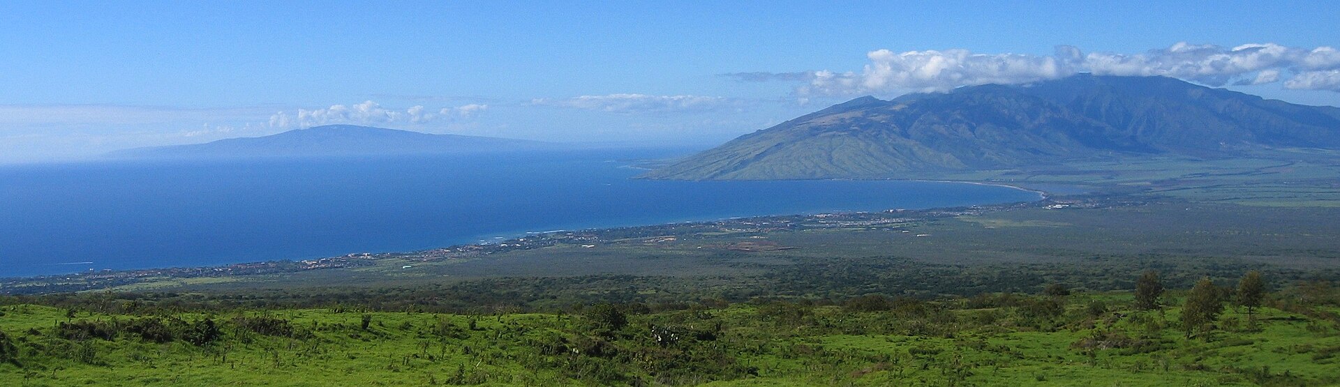 A wide view over green slopes to the ocean and the ridges of the West Maui Mountains.