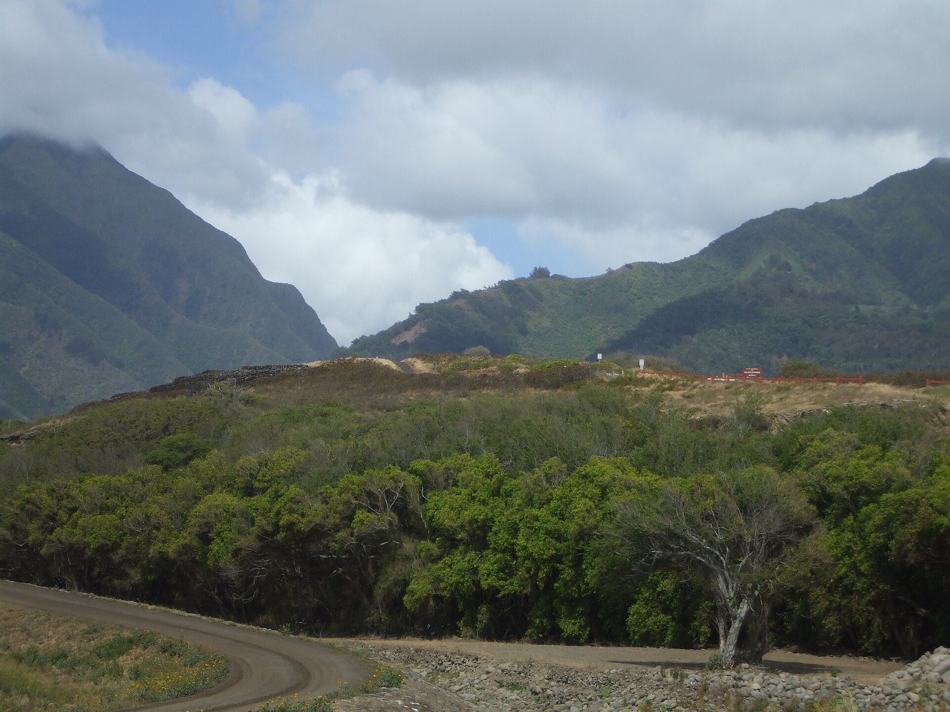 A grassy valley with mountains behind, the Haleki'i-Pihana Heiau State Monument in Waiehu, Hawaii.