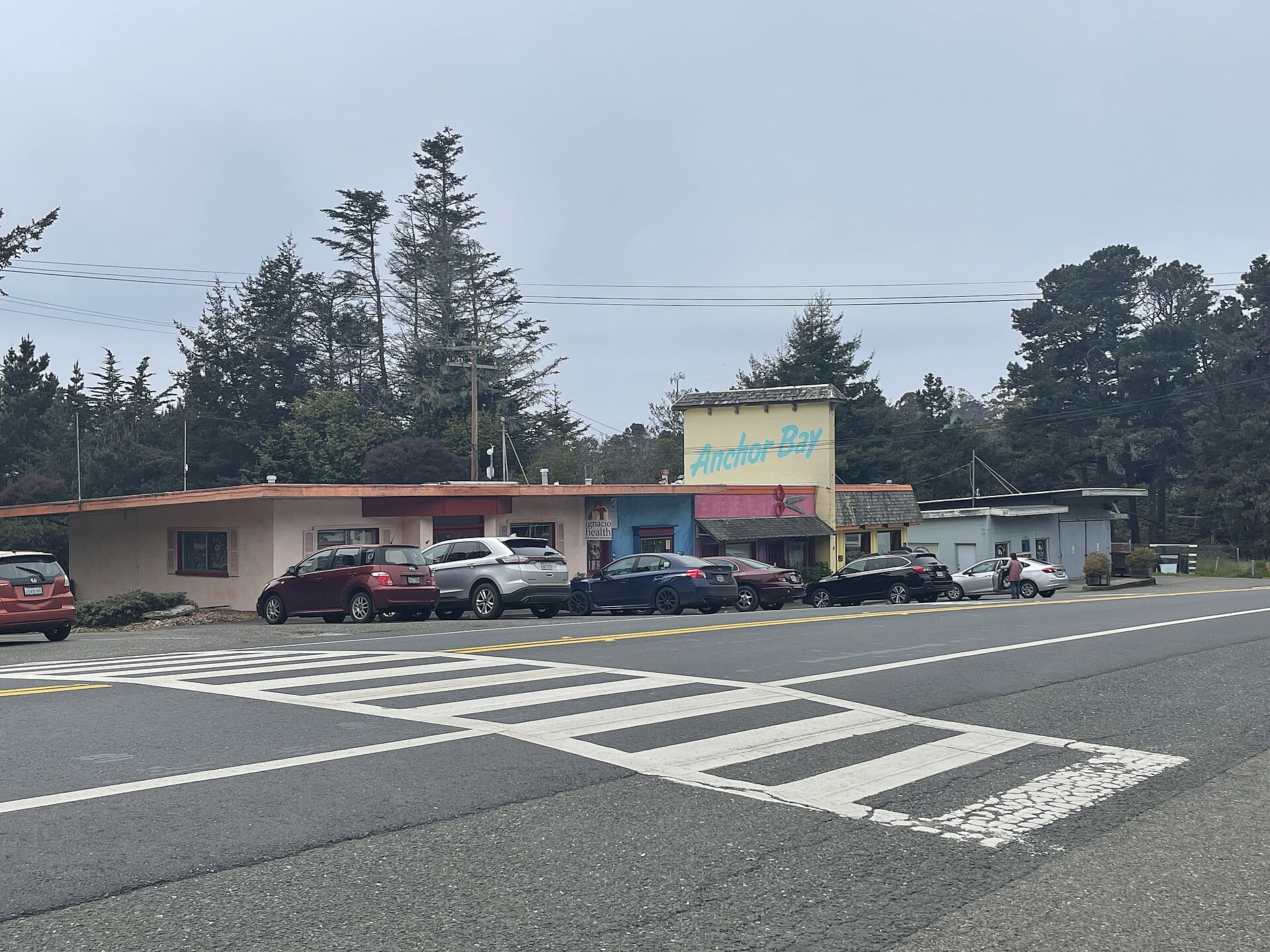 A low roadside building with an 'Anchor Bay' sign, parked cars, and tall pines behind.