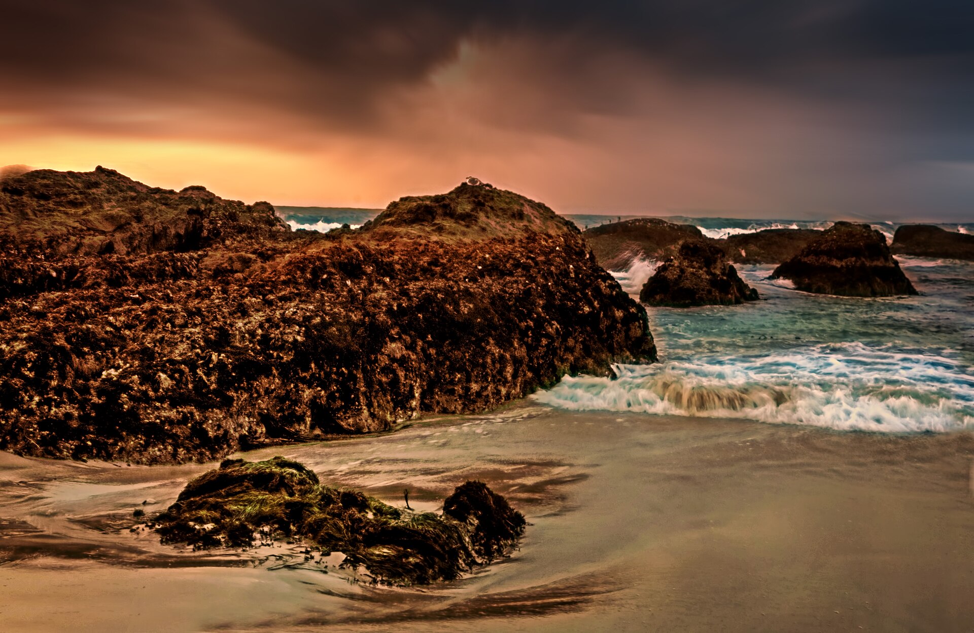 Waves crashing against dark sea rocks under a stormy sky at Glass Beach in Fort Bragg, California