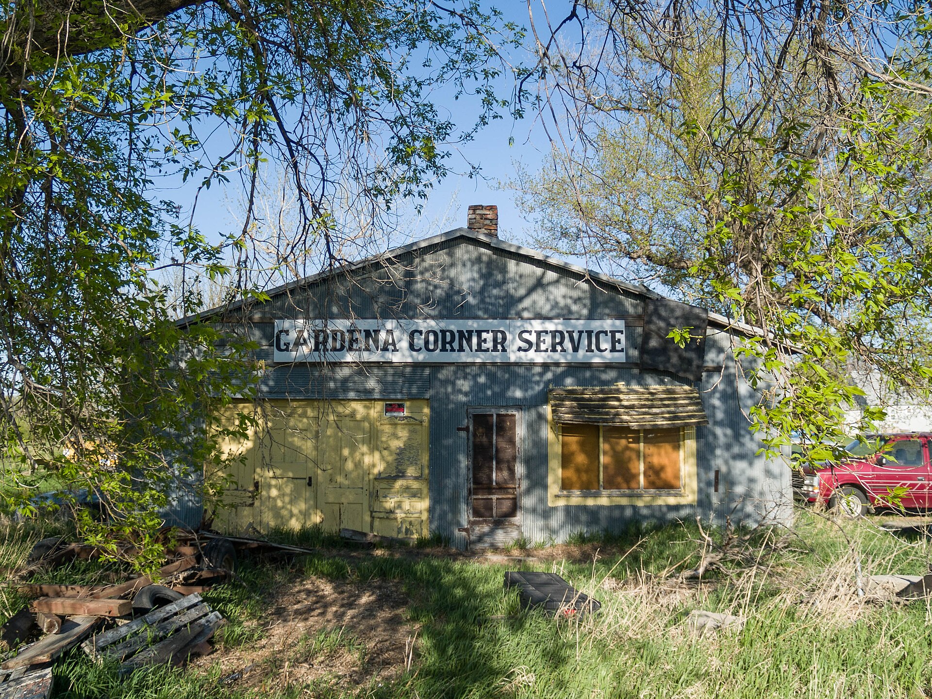 A weathered blue service station with hand-painted signage, surrounded by grass and trees.